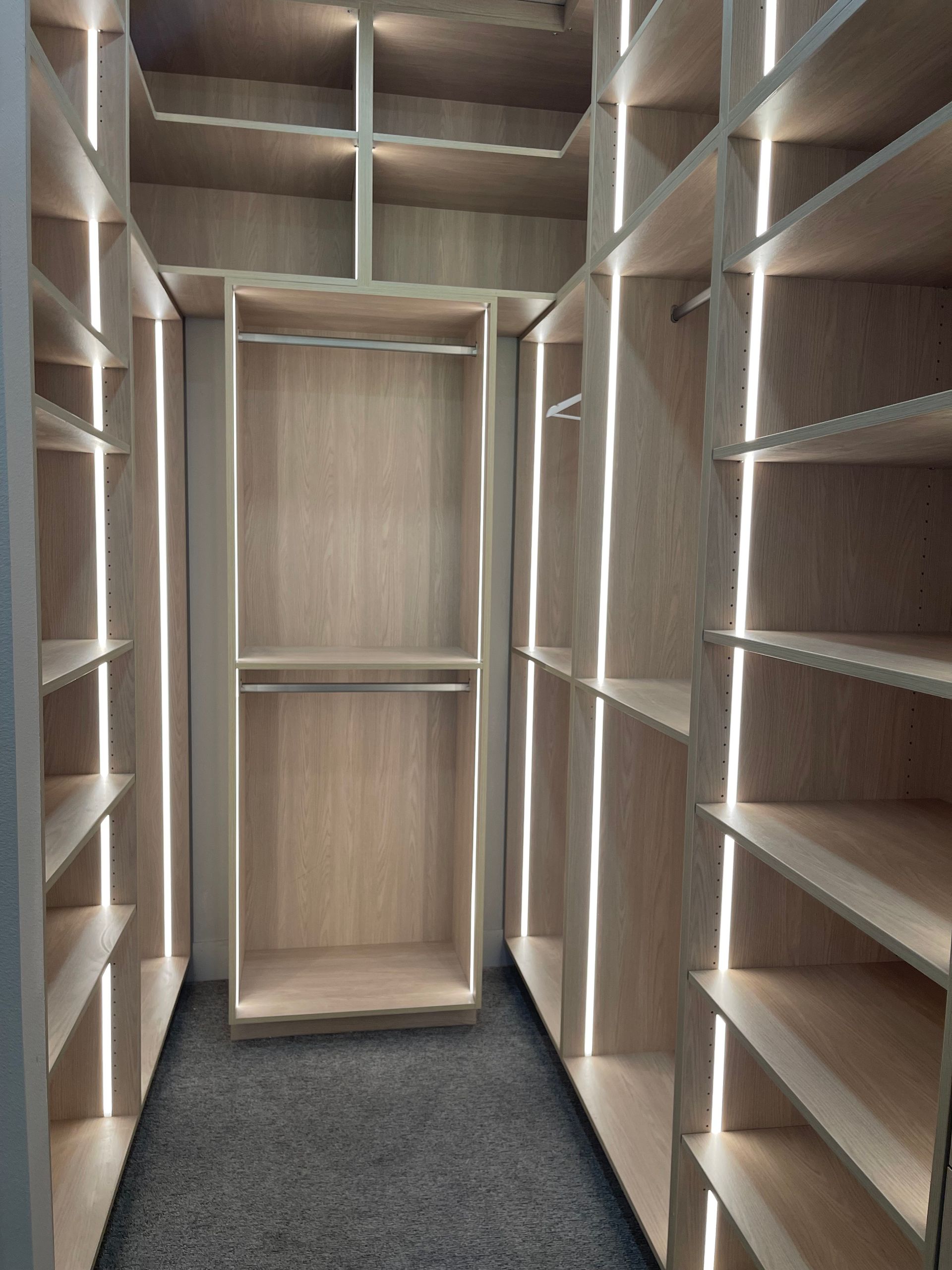 Walk-in closet with empty wooden shelves and hanging space, dark carpeted floor.