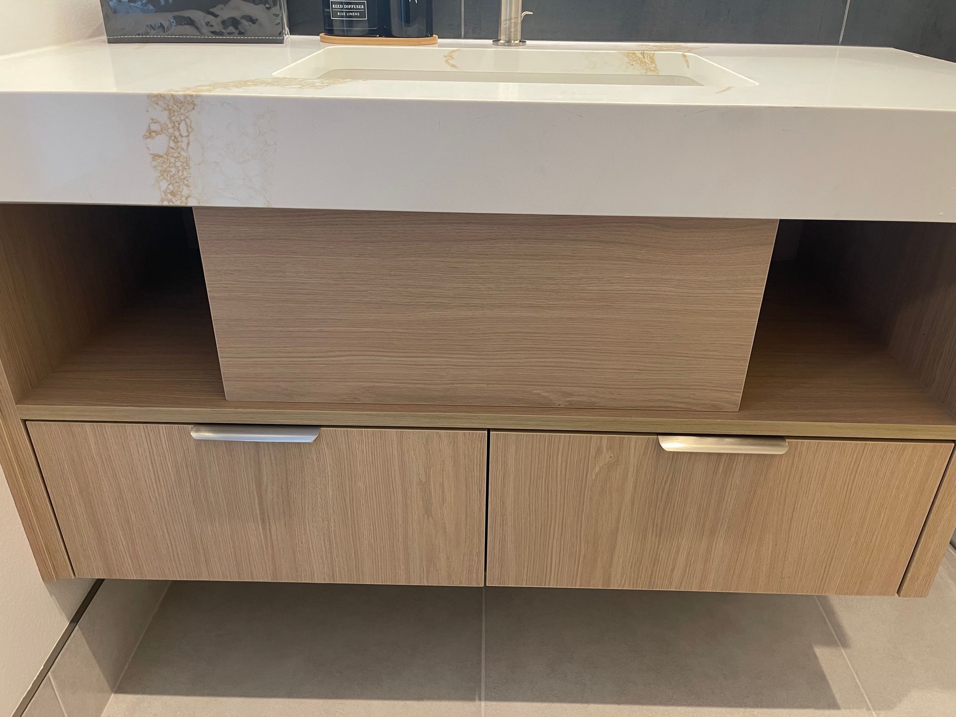 Bathroom vanity with two drawers and open shelves, light wood finish, white countertop, and silver handles.