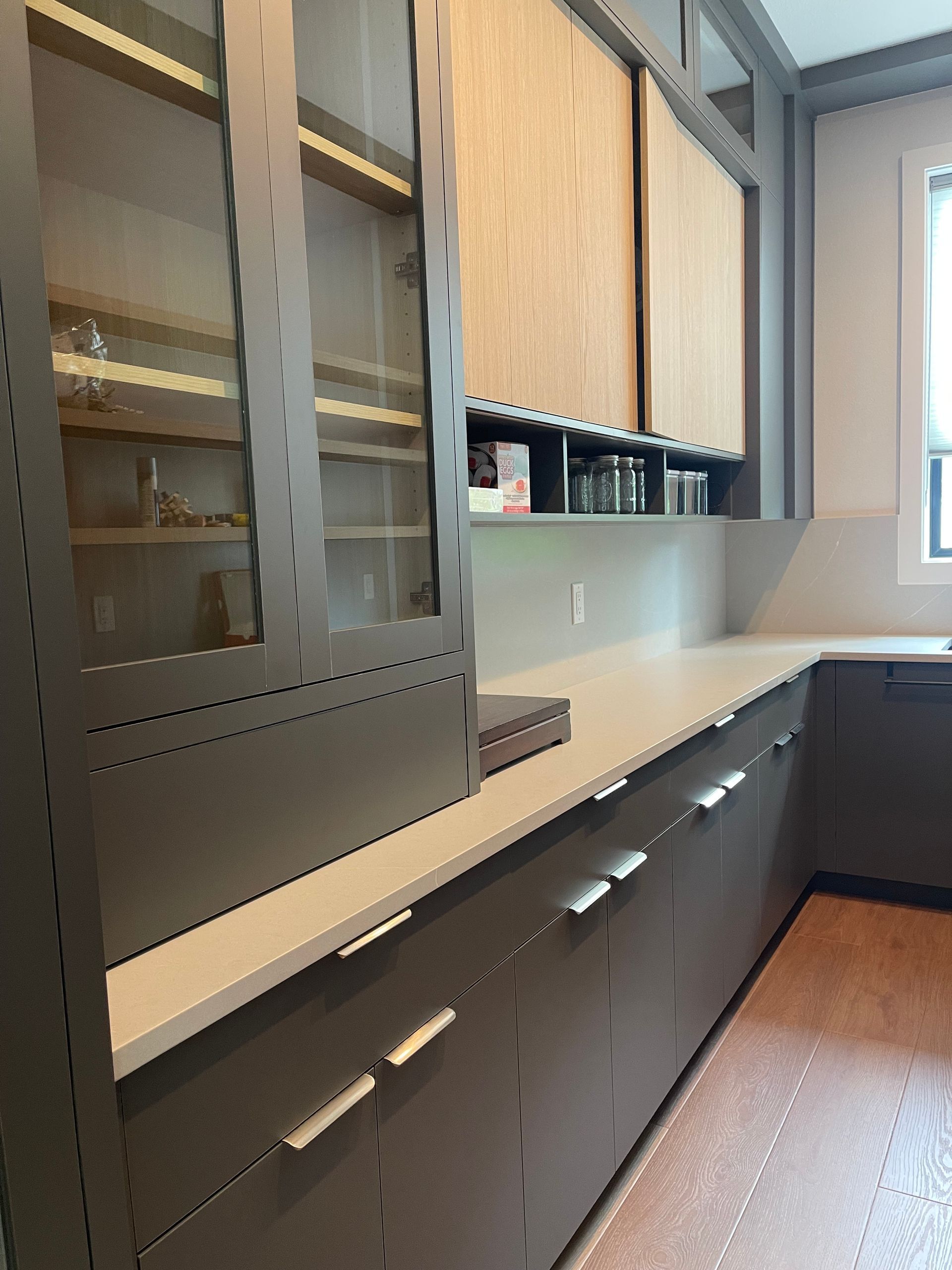 Modern kitchen with gray cabinets, glass-fronted display, and light countertops.