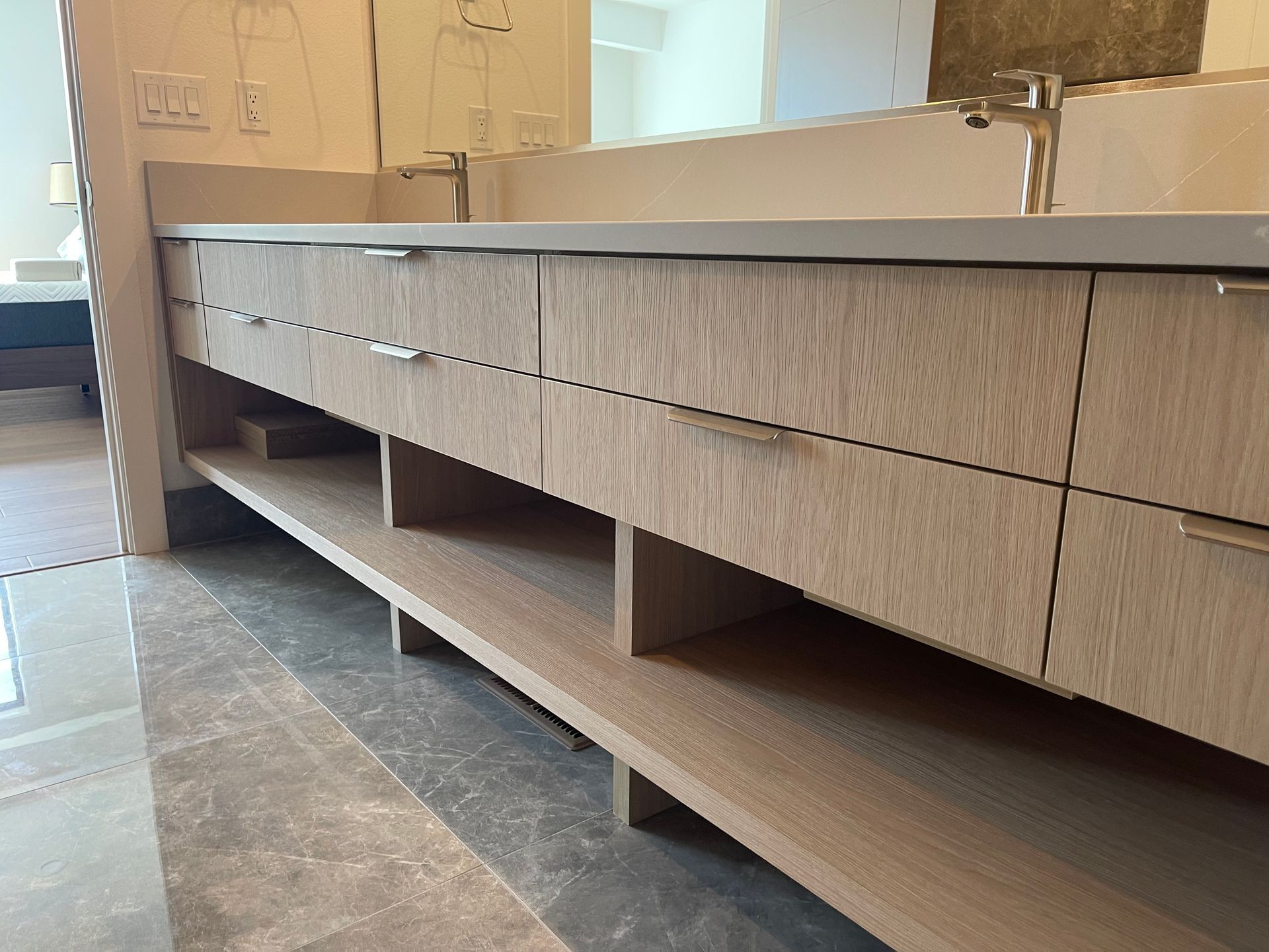 Light wood bathroom vanity with open shelving and drawers, against a light-colored wall.