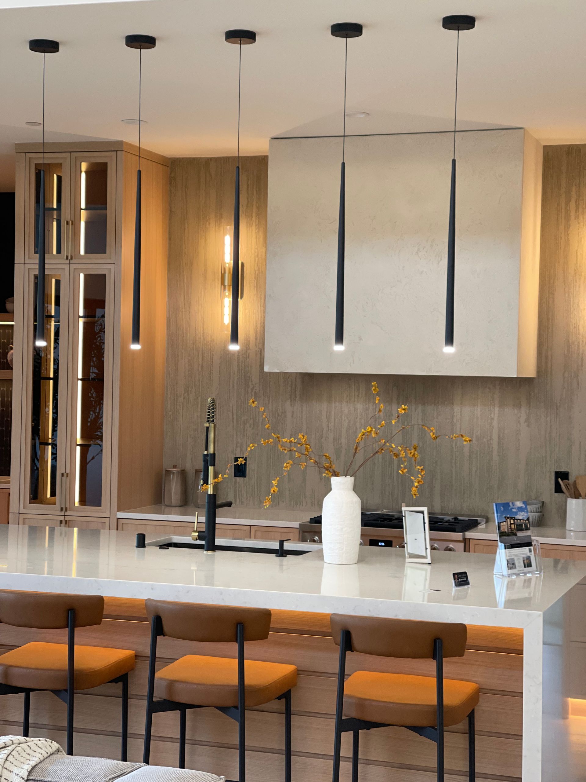 Modern kitchen with white island, wooden bar stools, pendant lights, and warm wood accents
