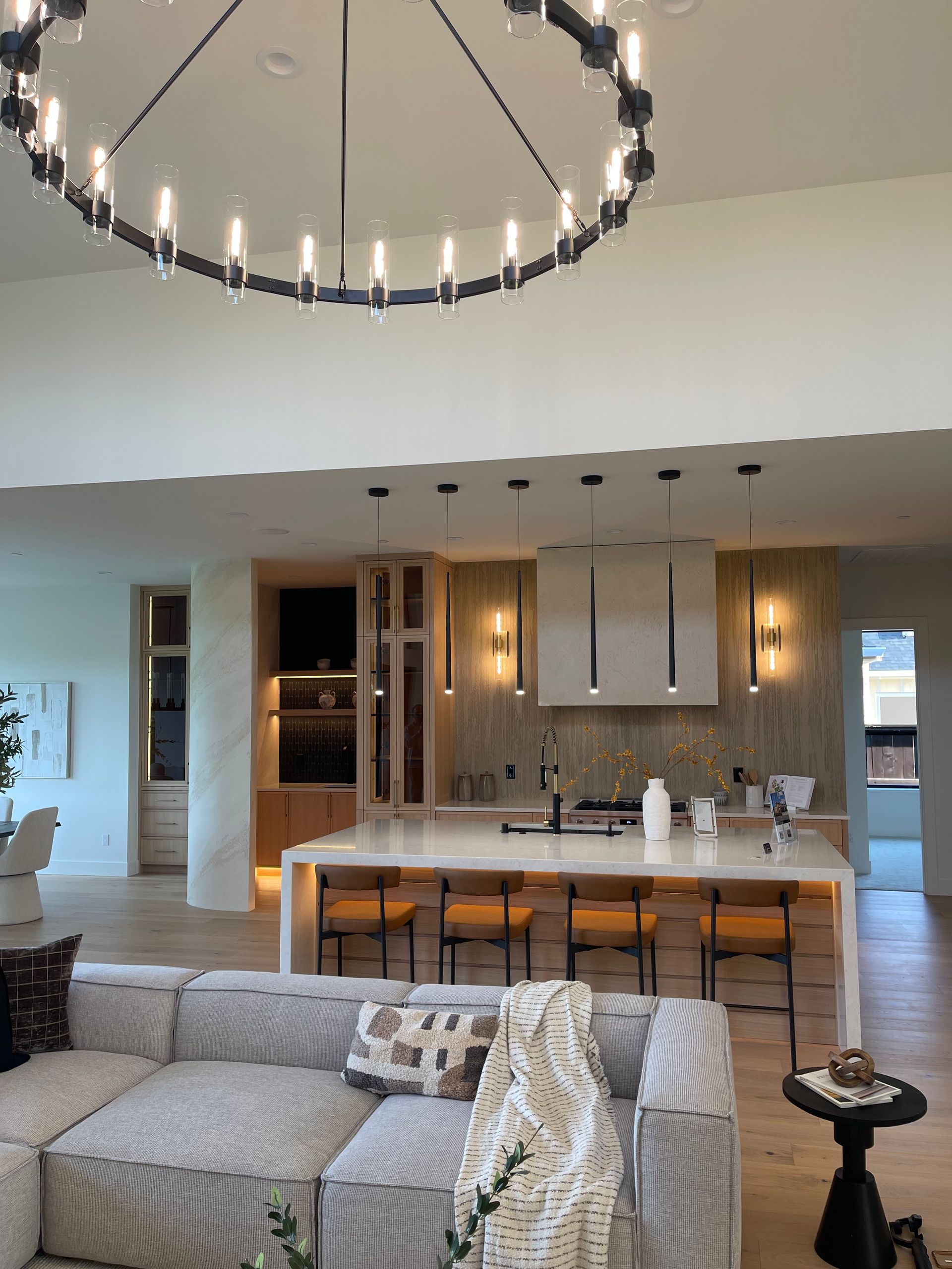 Modern open-concept living room and kitchen with gray sofa, island seating, and large circular chandelier