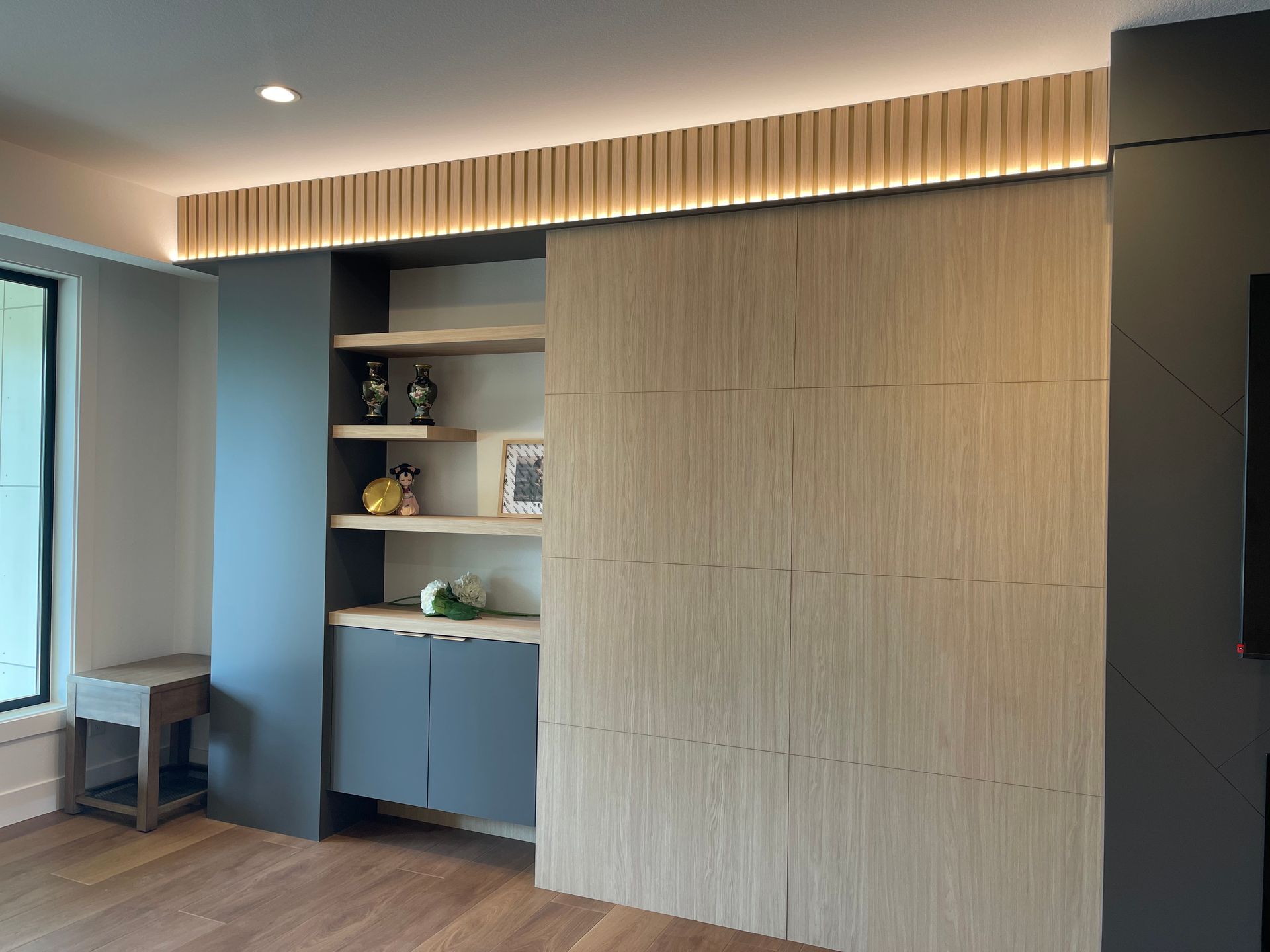 Modern room with built-in wood cabinetry, blue shelves, a window seat, and warm ceiling lighting.