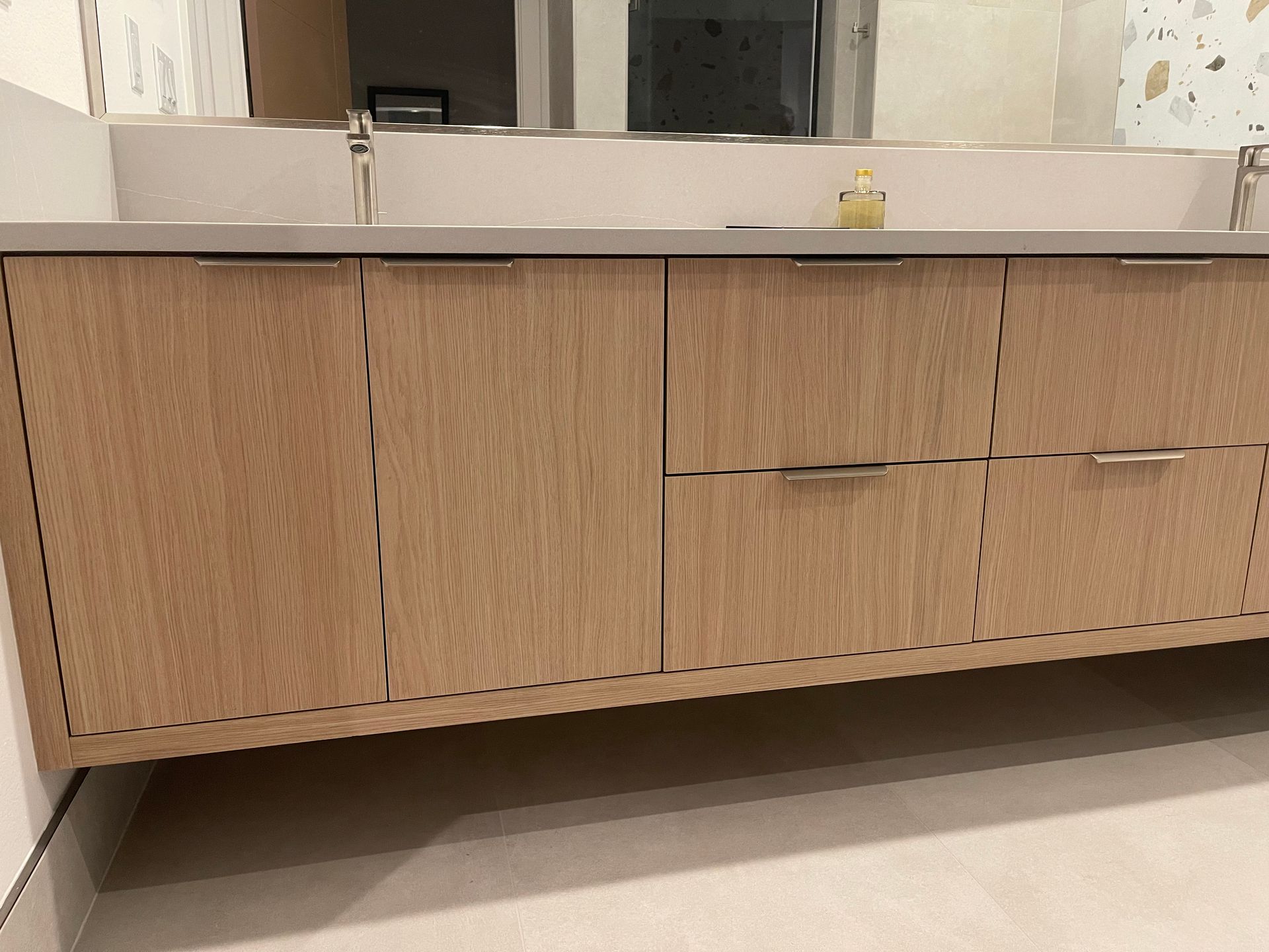 Wooden bathroom vanity with two doors and two drawers, under a light countertop and mirrors.