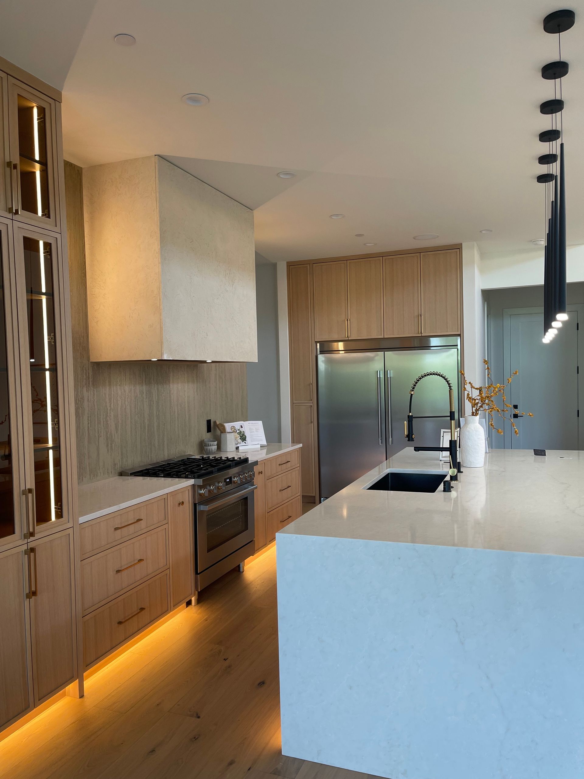 Modern kitchen with white island, wood cabinets, black pendant lights, and warm under-cabinet lighting