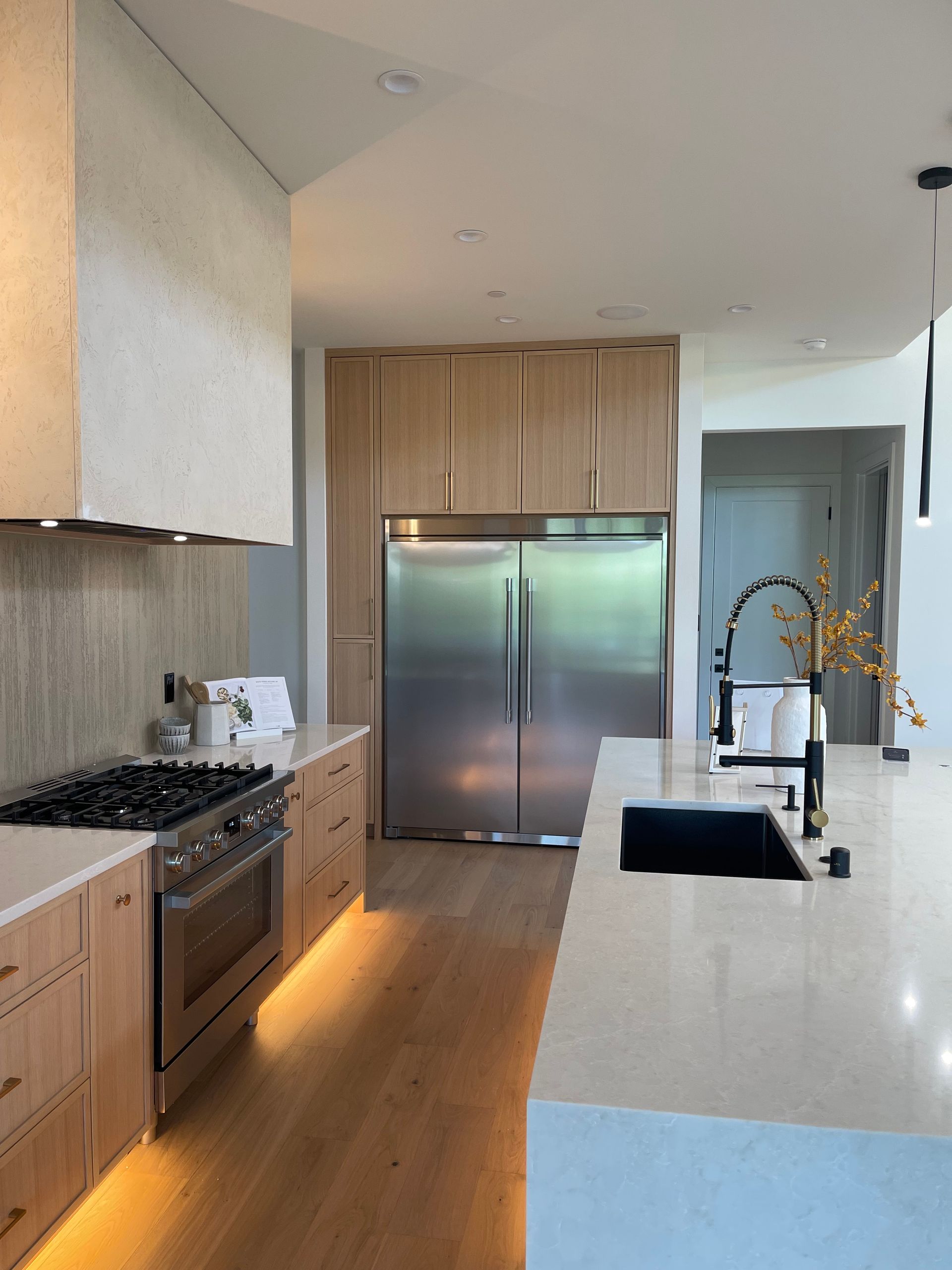 Modern kitchen with stainless steel appliances, light wood cabinets, and a large island with a sink.