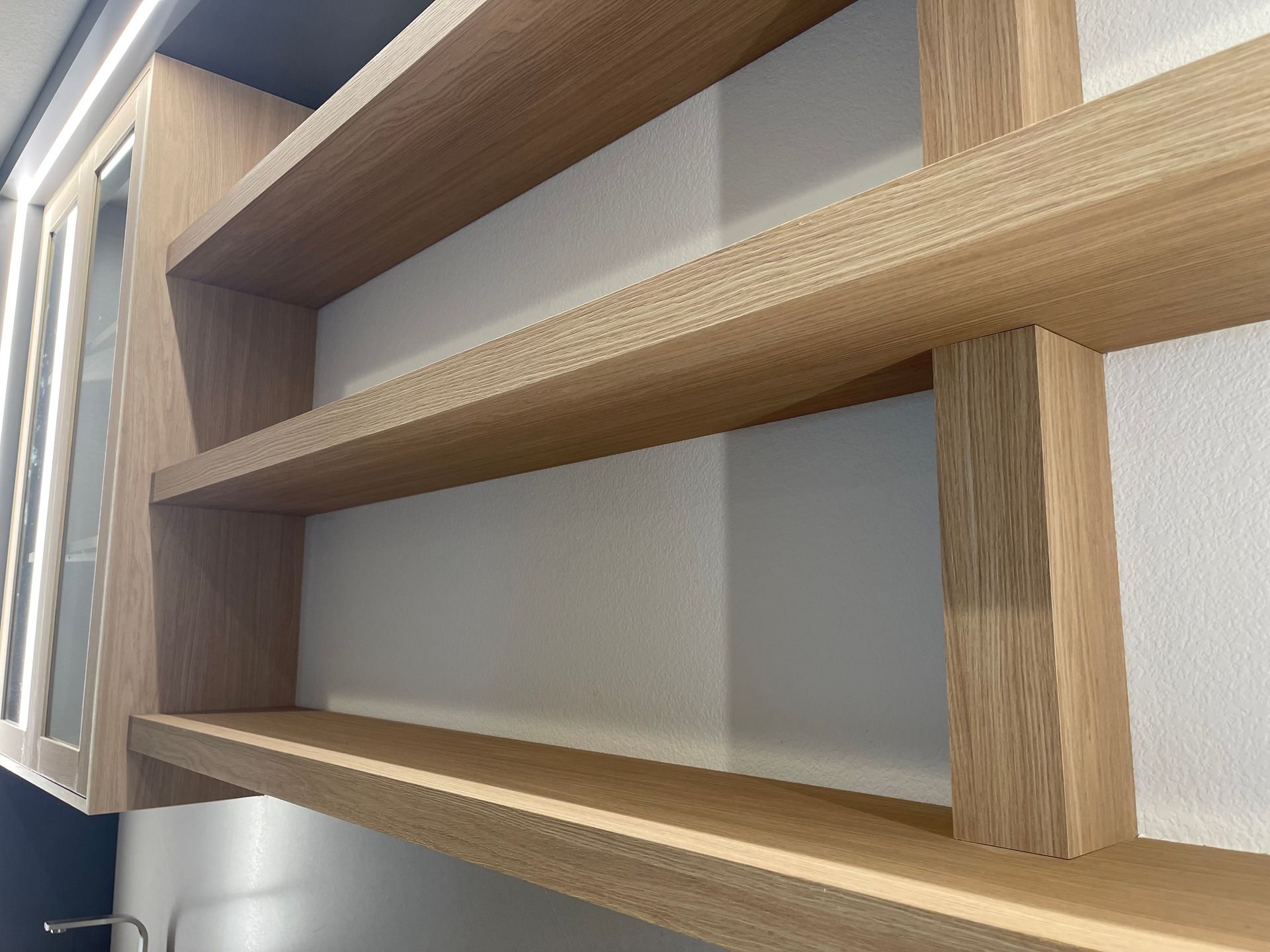 Wooden shelves built into a wall, next to a glass cabinet.