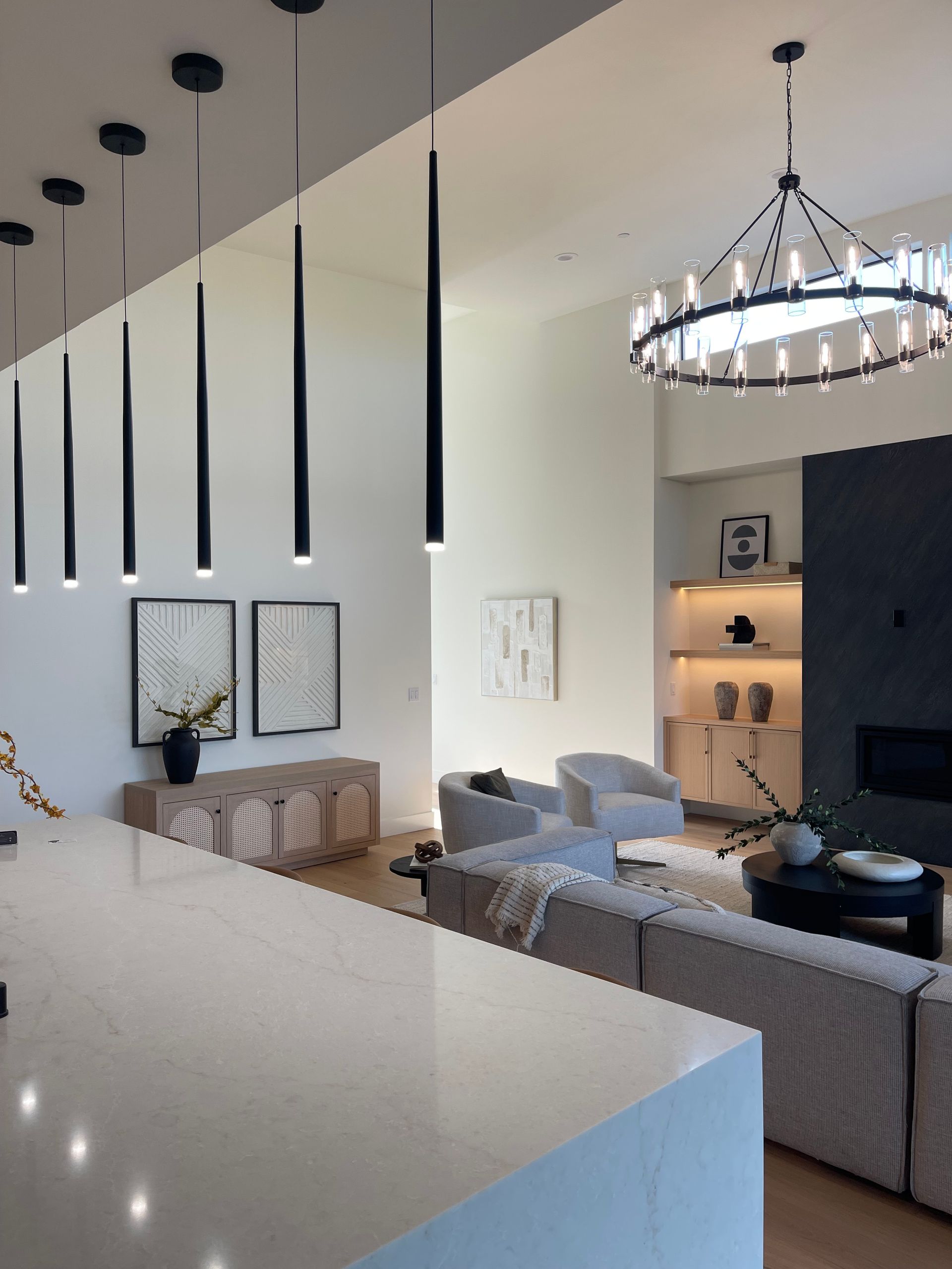 Modern open-concept living room with gray sofas, black chandelier, and minimalist wall art