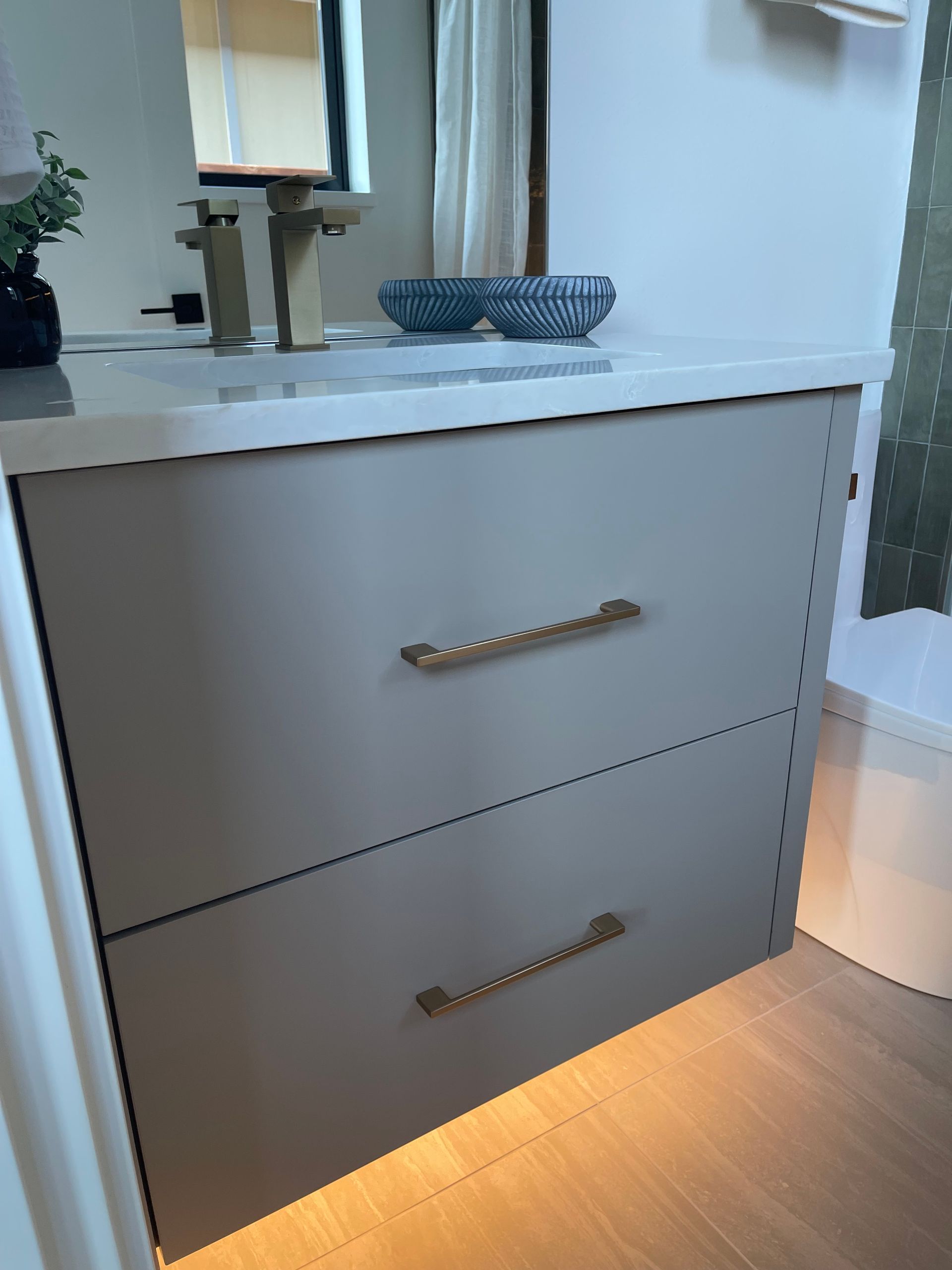White bathroom vanity with two drawers, countertop sink, and warm floor lighting near a mirror