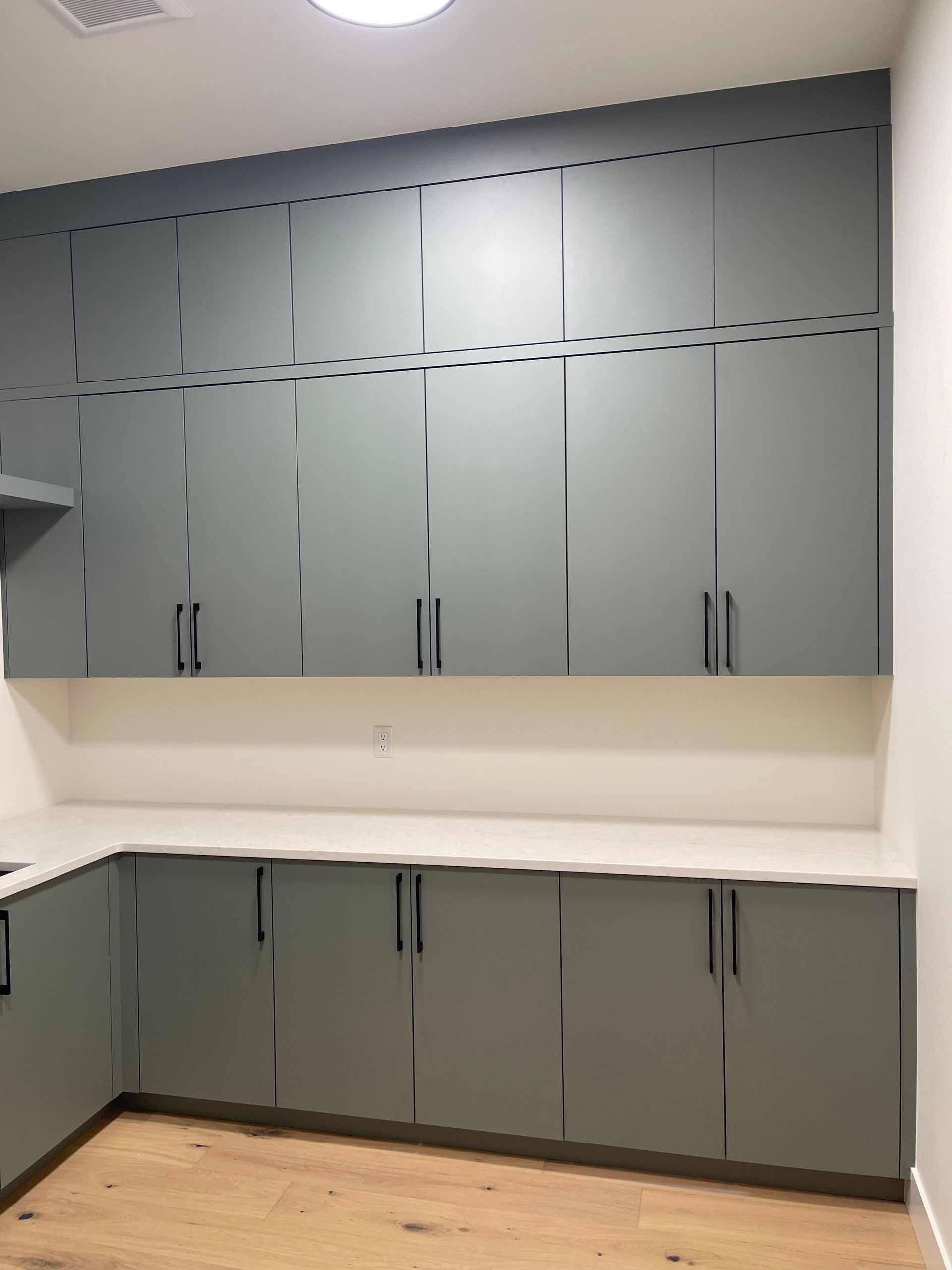 Gray cabinets in a utility room with a white countertop and wood floor.