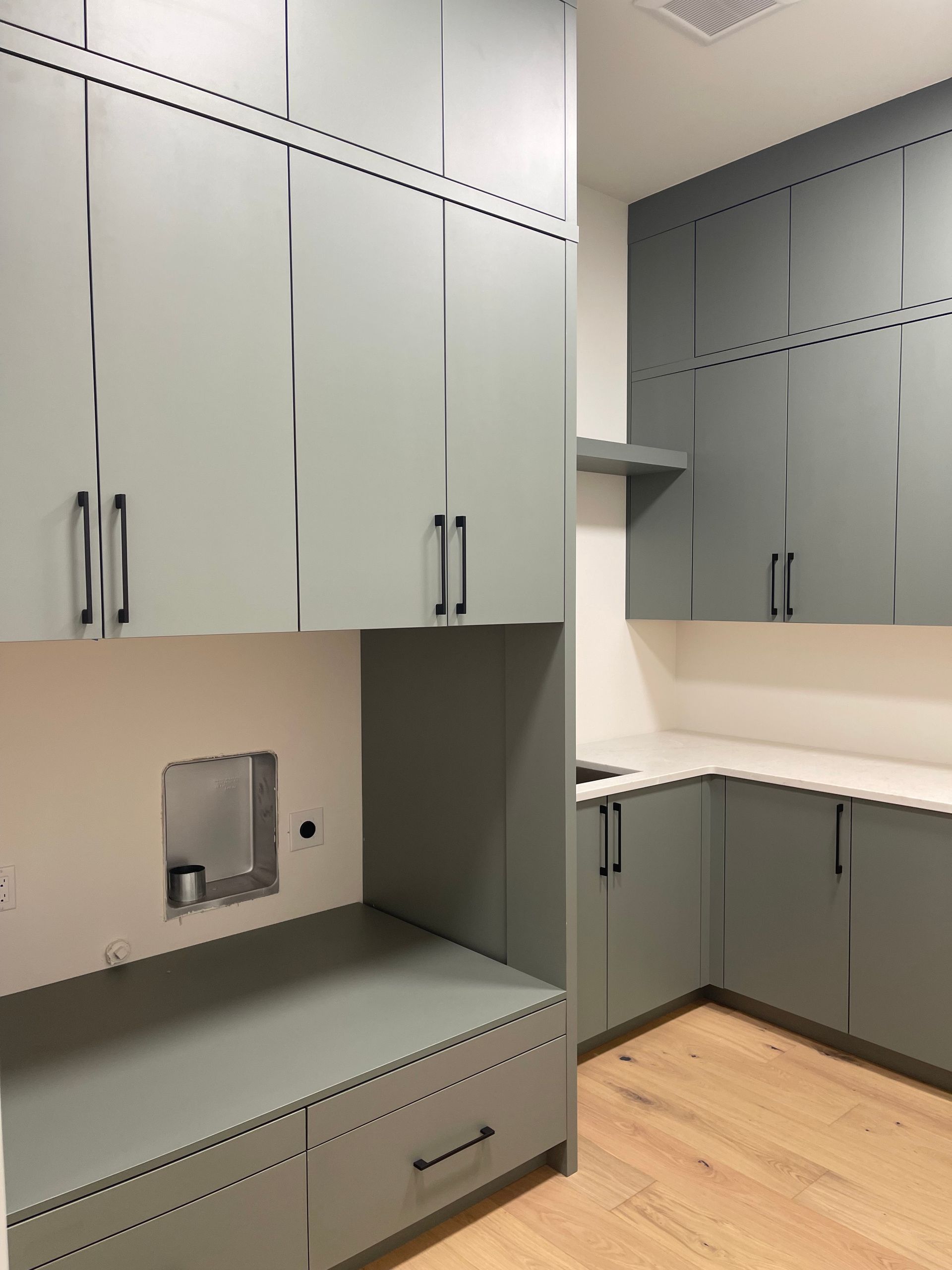 Built-in gray cabinets and drawers in a modern empty office or utility room with light wood flooring