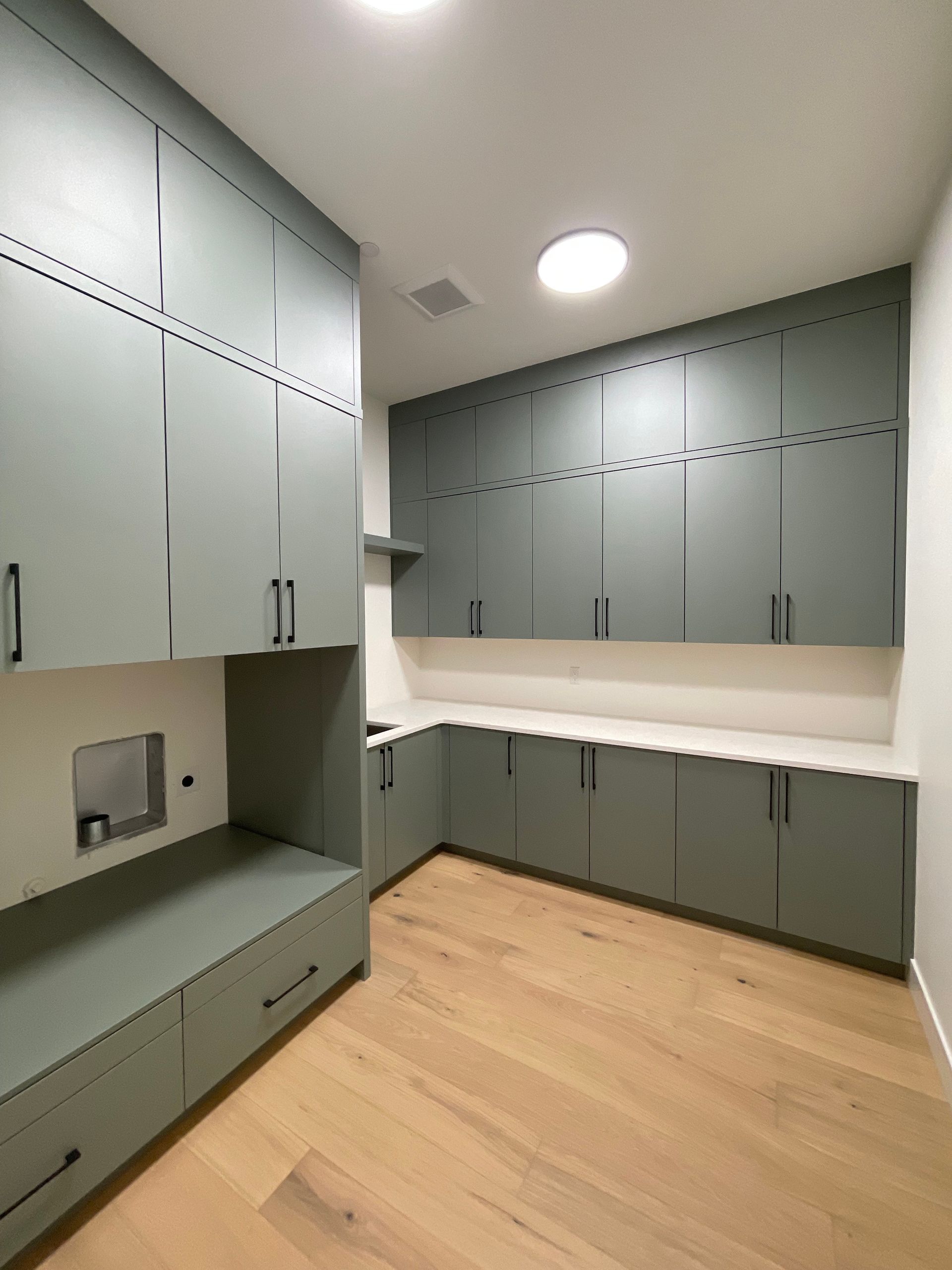 Modern empty kitchen with gray cabinets, white countertops, and light wood flooring.