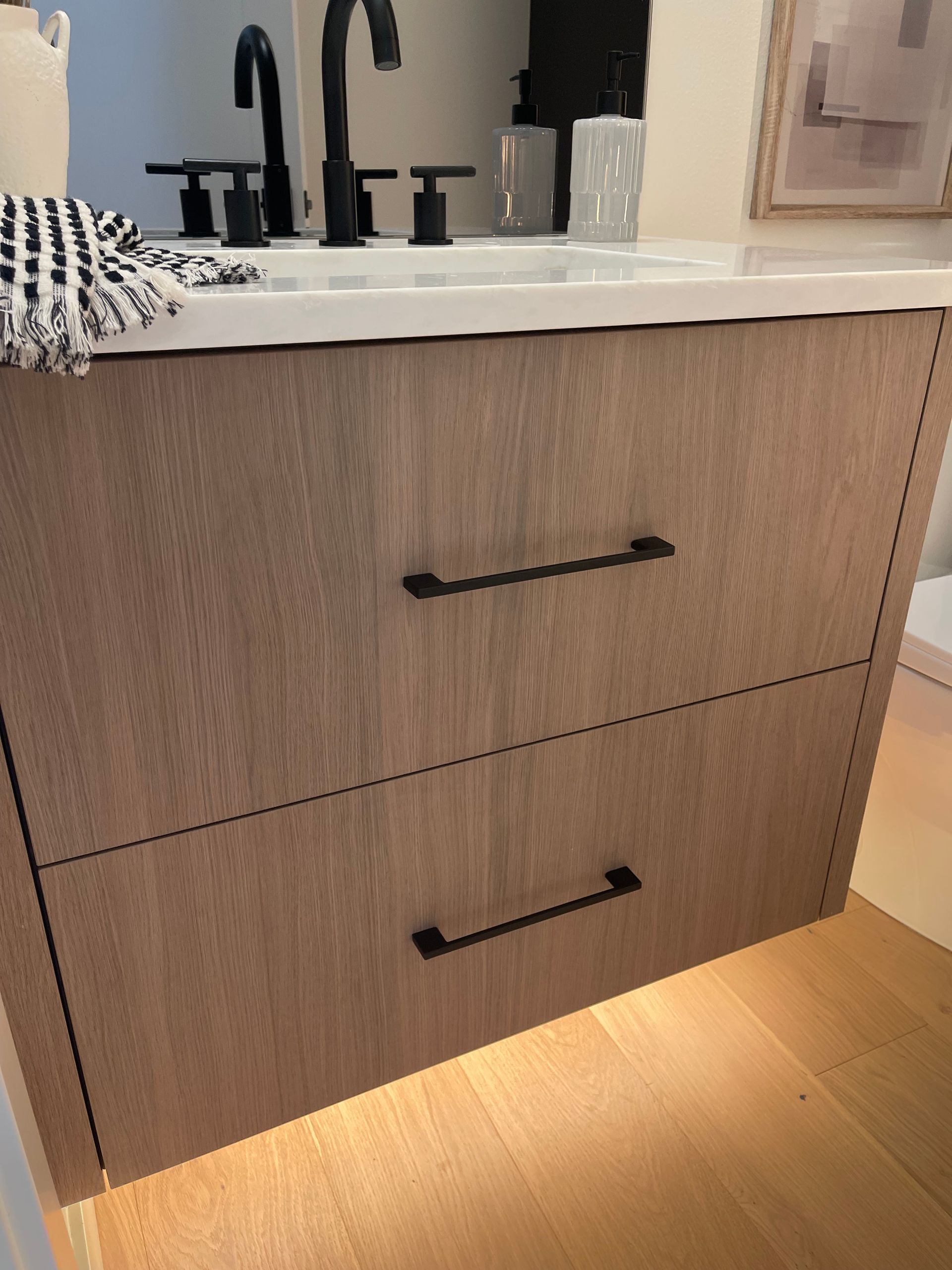 Modern bathroom vanity with wood drawers, black handles, and warm under-cabinet lighting