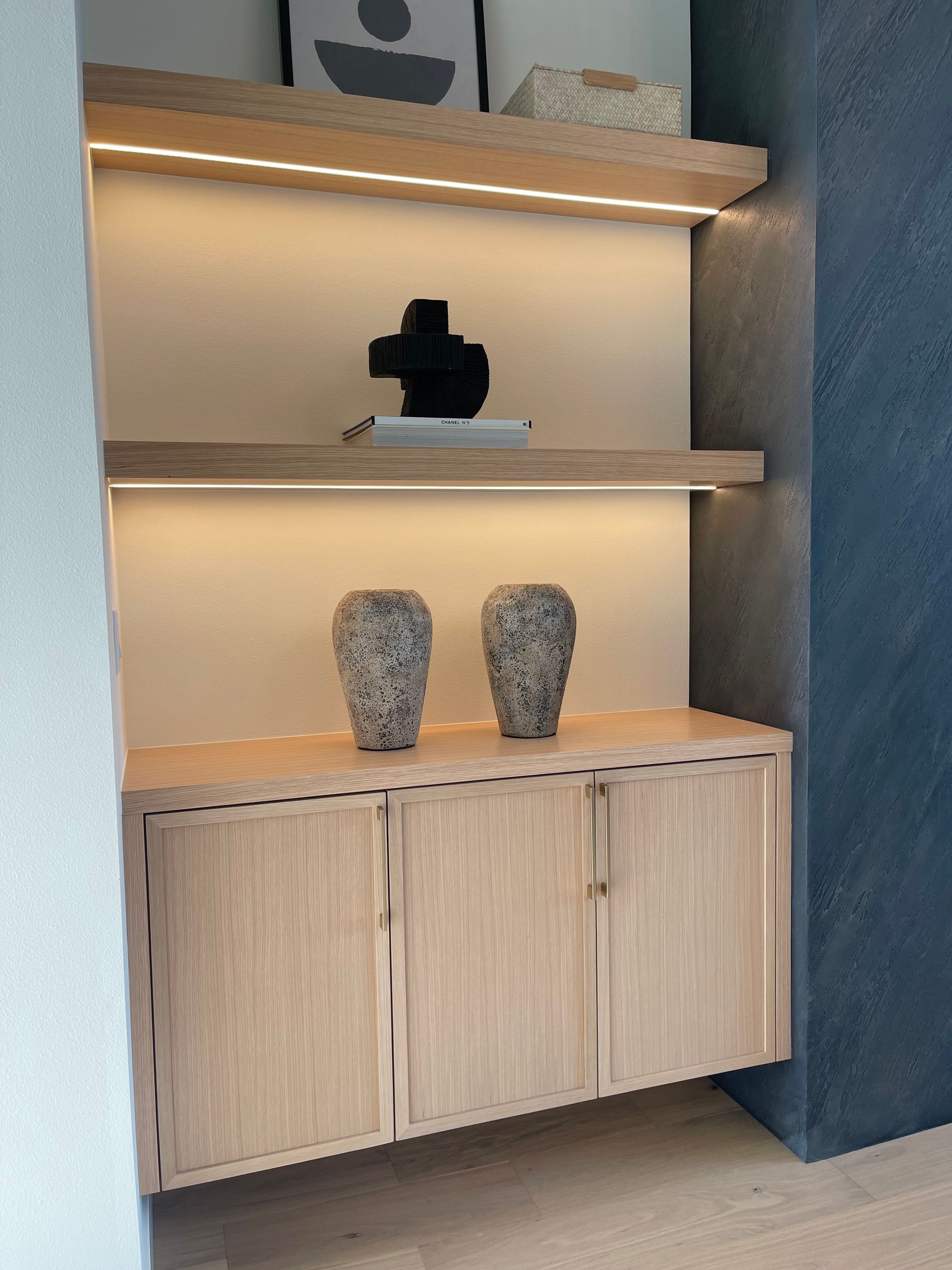 Built-in wood shelving with decorative vases and a black sculpture, lit by warm under-shelf lighting.