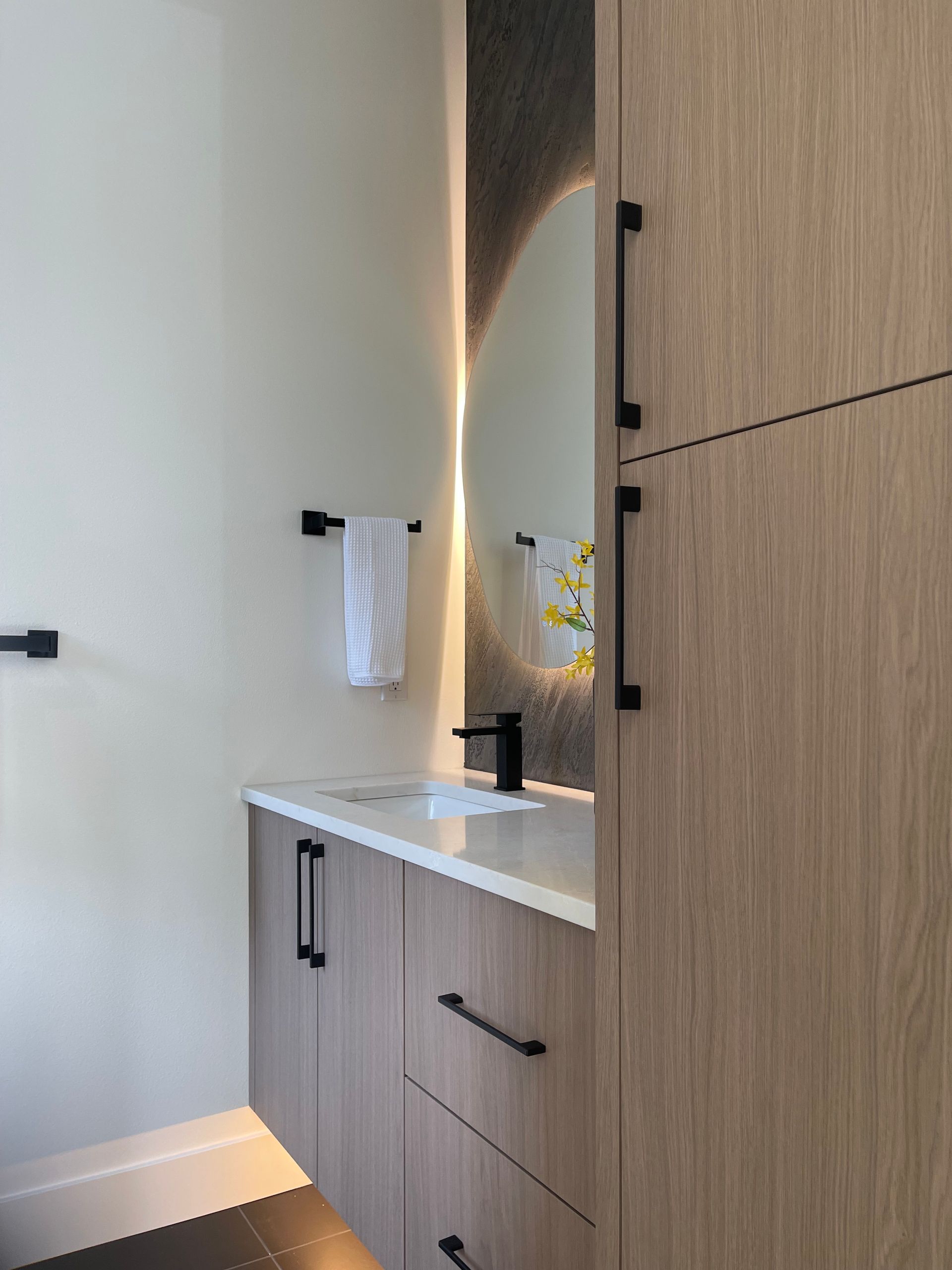 Modern bathroom vanity with light wood cabinets, white countertop, mirror, and black fixtures.