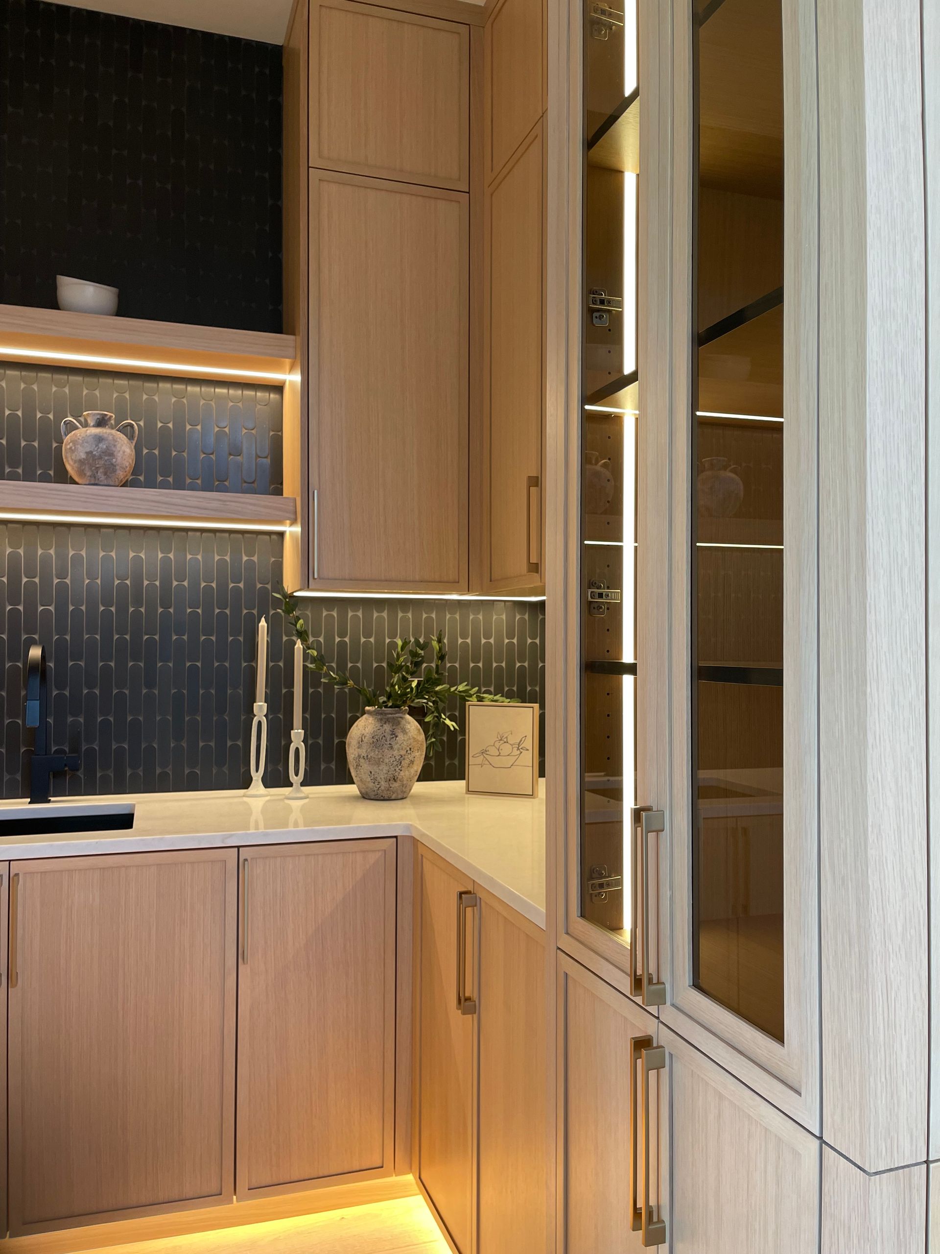 Modern kitchen corner with wood cabinets, glass-front pantry, and under-cabinet lighting