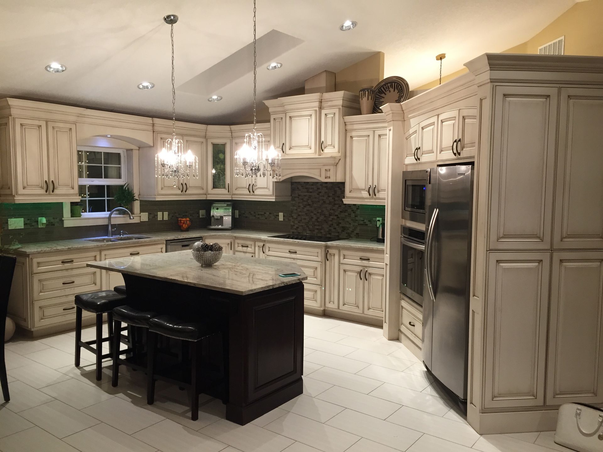 Cream-colored kitchen cabinets with dark island and stainless steel appliances; a chandelier hangs over the island.