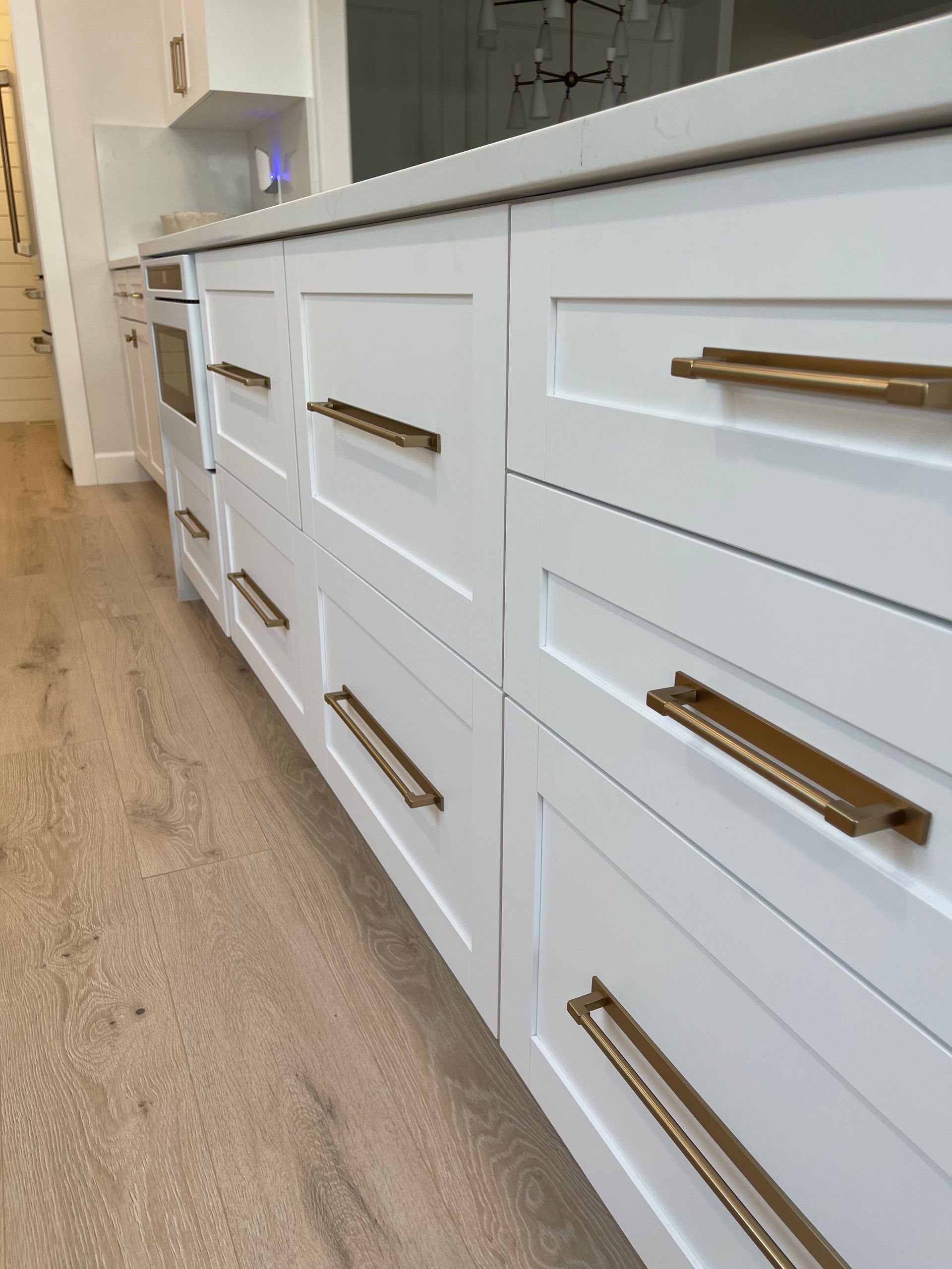 White kitchen cabinets with gold handles along a hallway floor