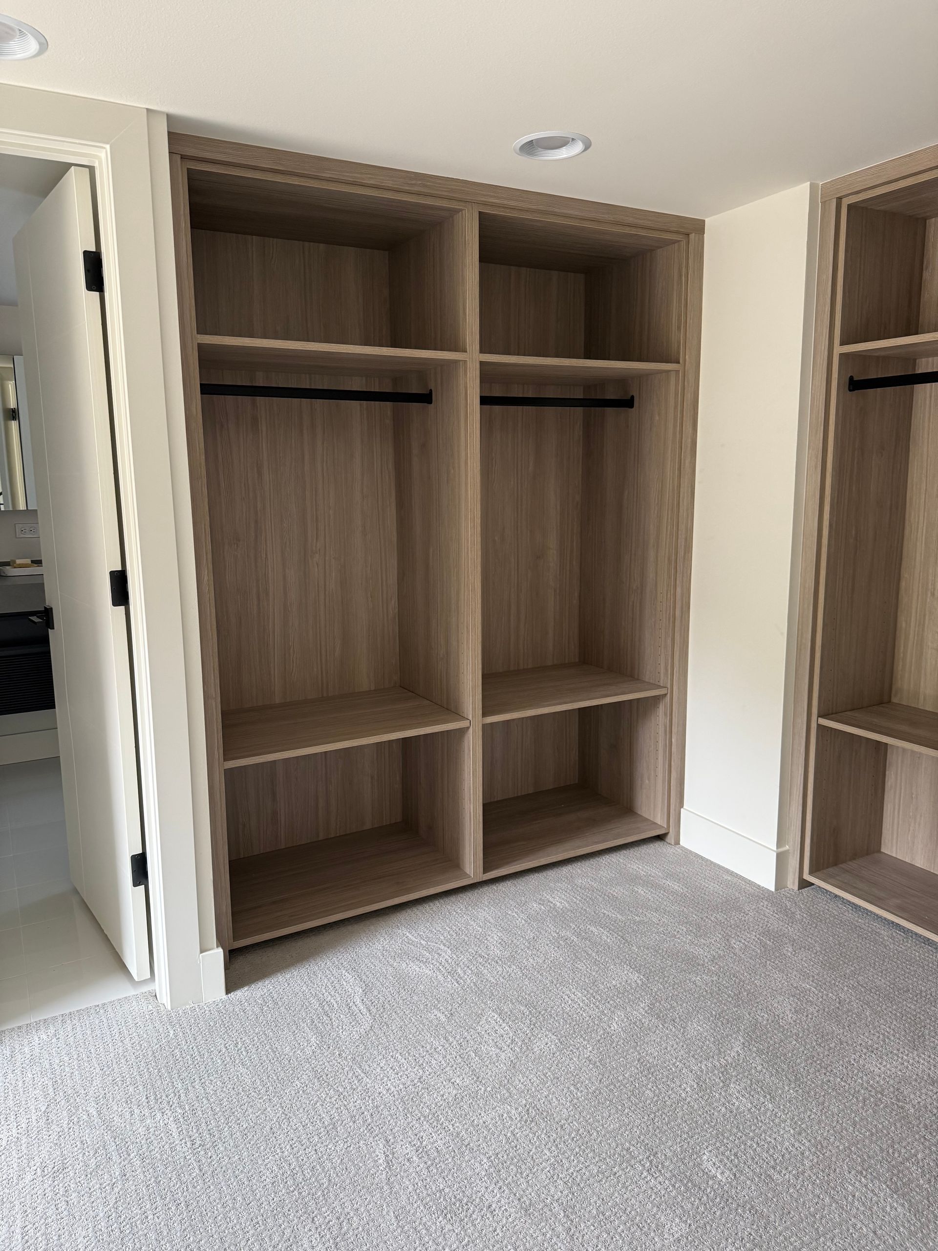 Built-in closet with shelves and hanging rods, neutral wood tone, on gray carpet.