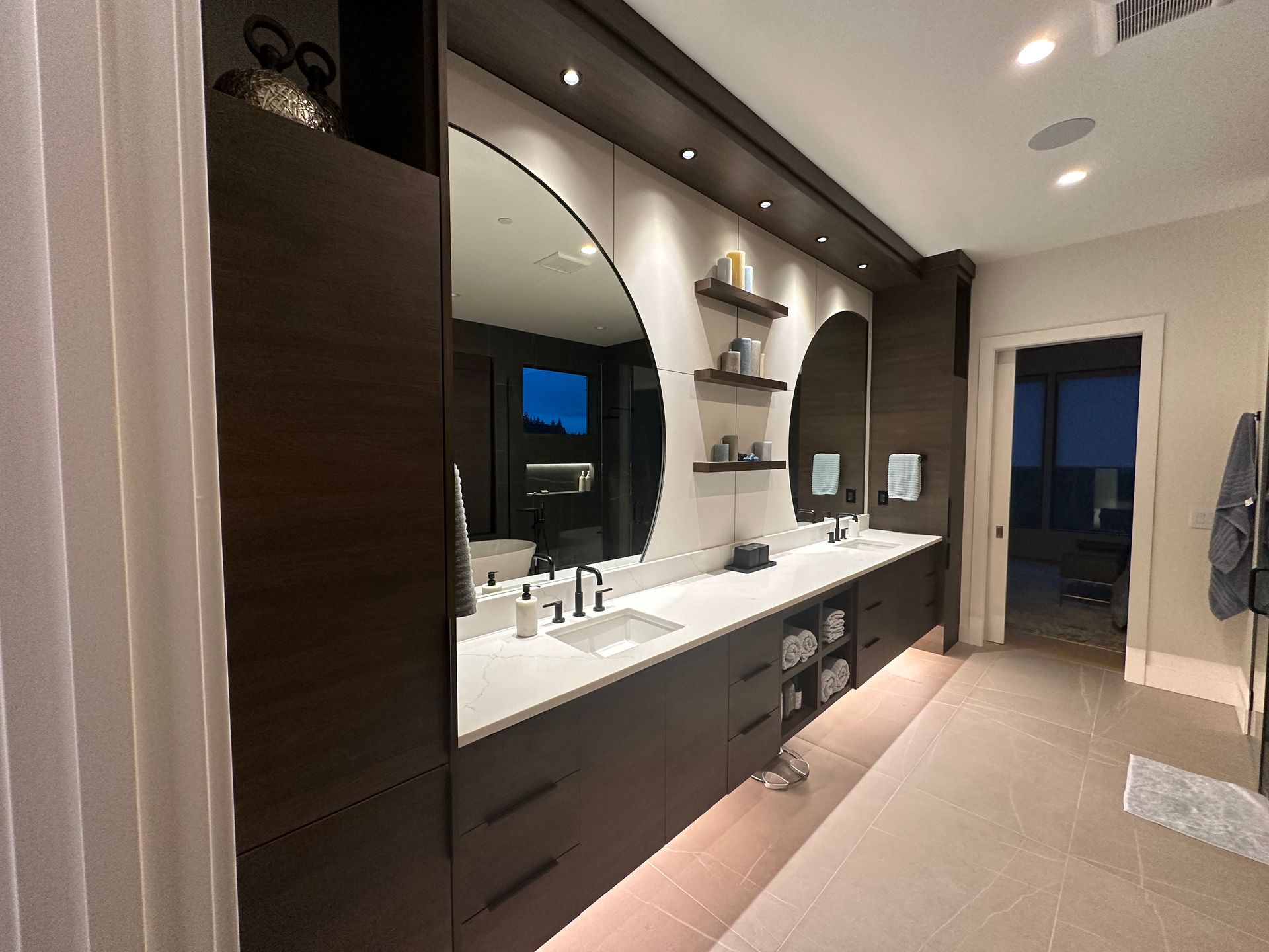 Modern bathroom with dark wood cabinetry, white countertops, large mirrors, and recessed lighting.