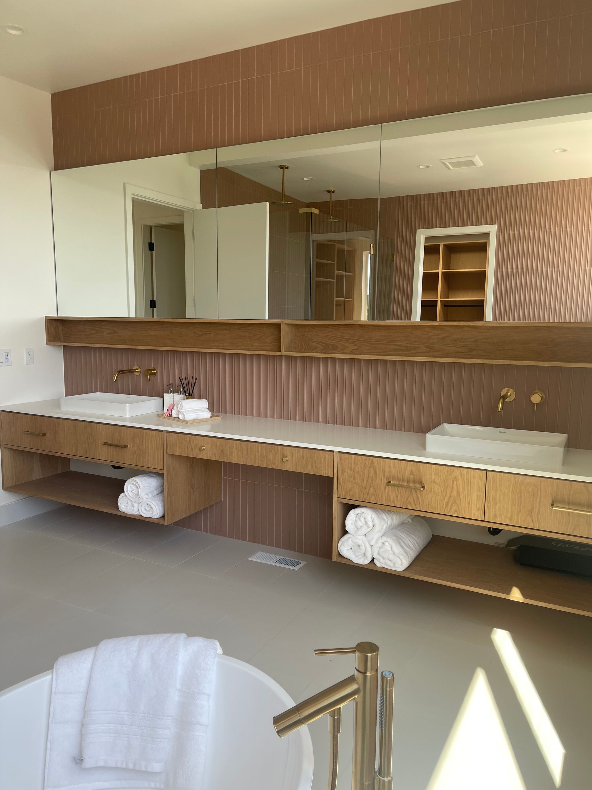 Bathroom with double sink vanity, large mirror, and soaking tub. Light wood, white and gold accents.
