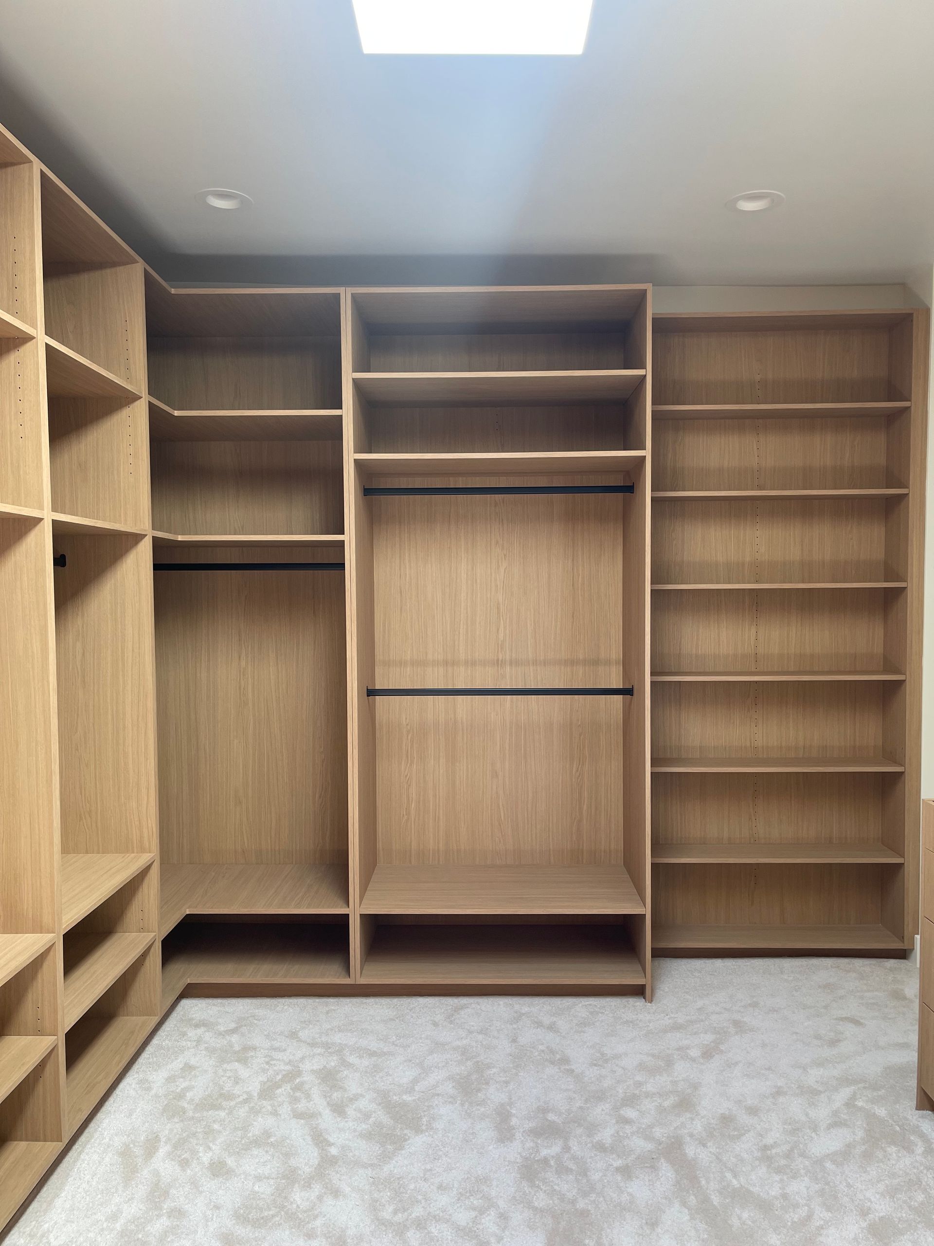 Light wood closet organization with shelving, hanging rods, and a neutral carpet.