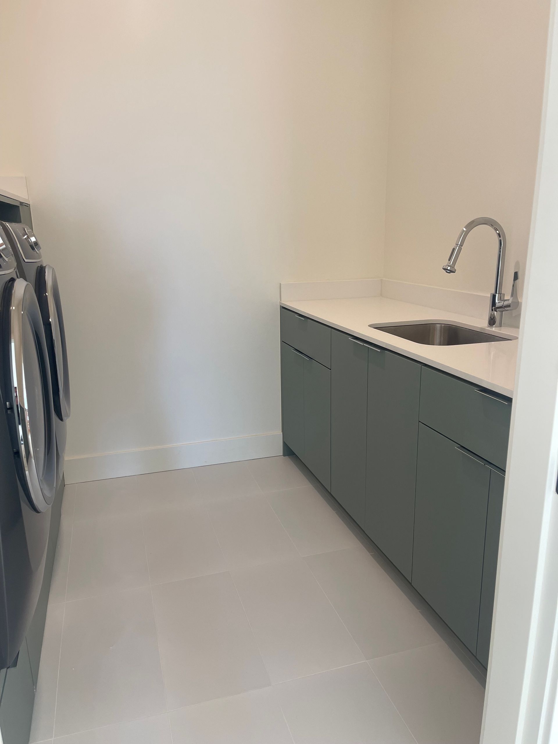 Laundry room with washer, sink, gray cabinets, and light tile floor.