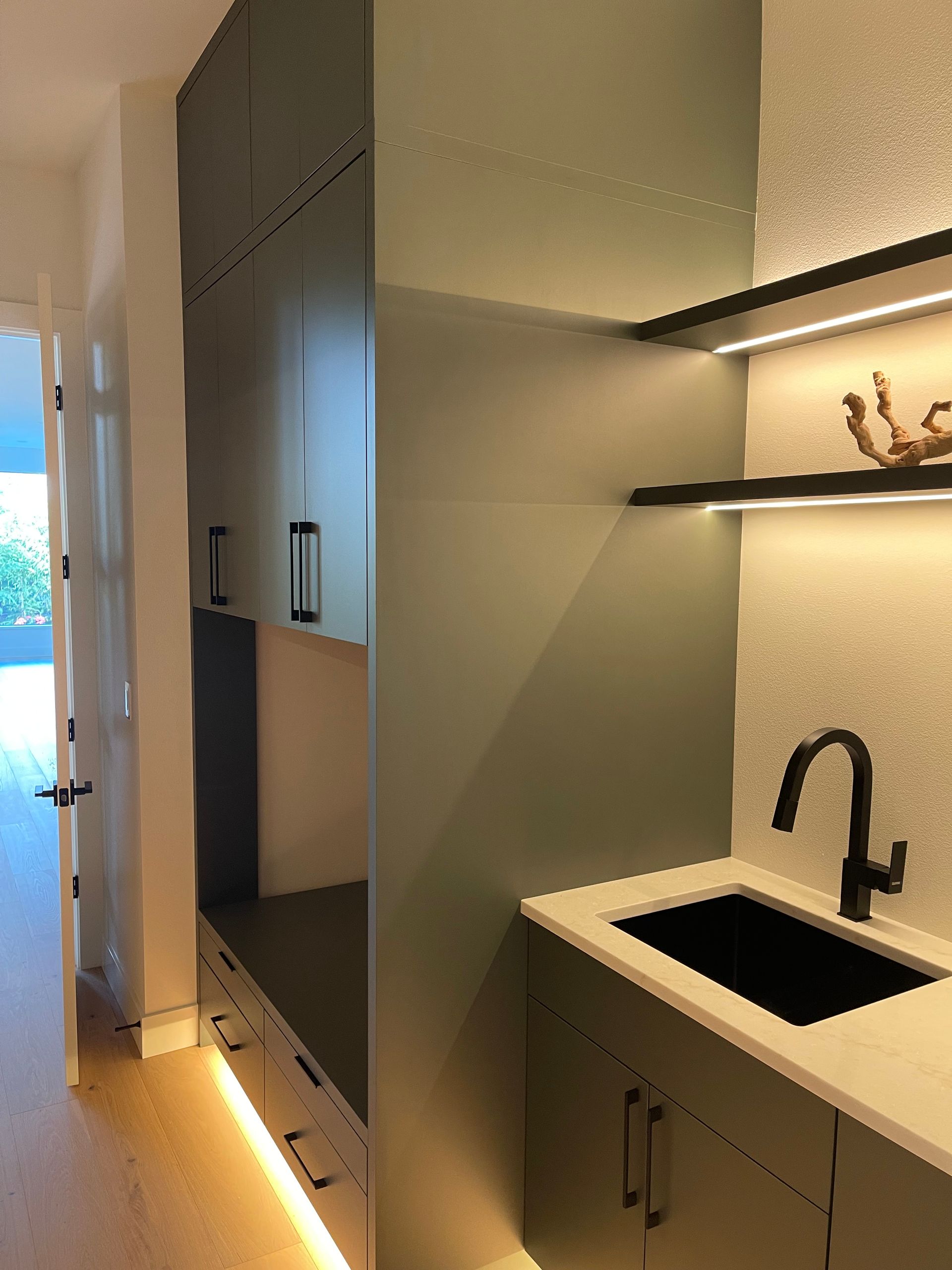 Modern laundry kitchenette with sink, matte black faucet, and open shelving beside a doorway