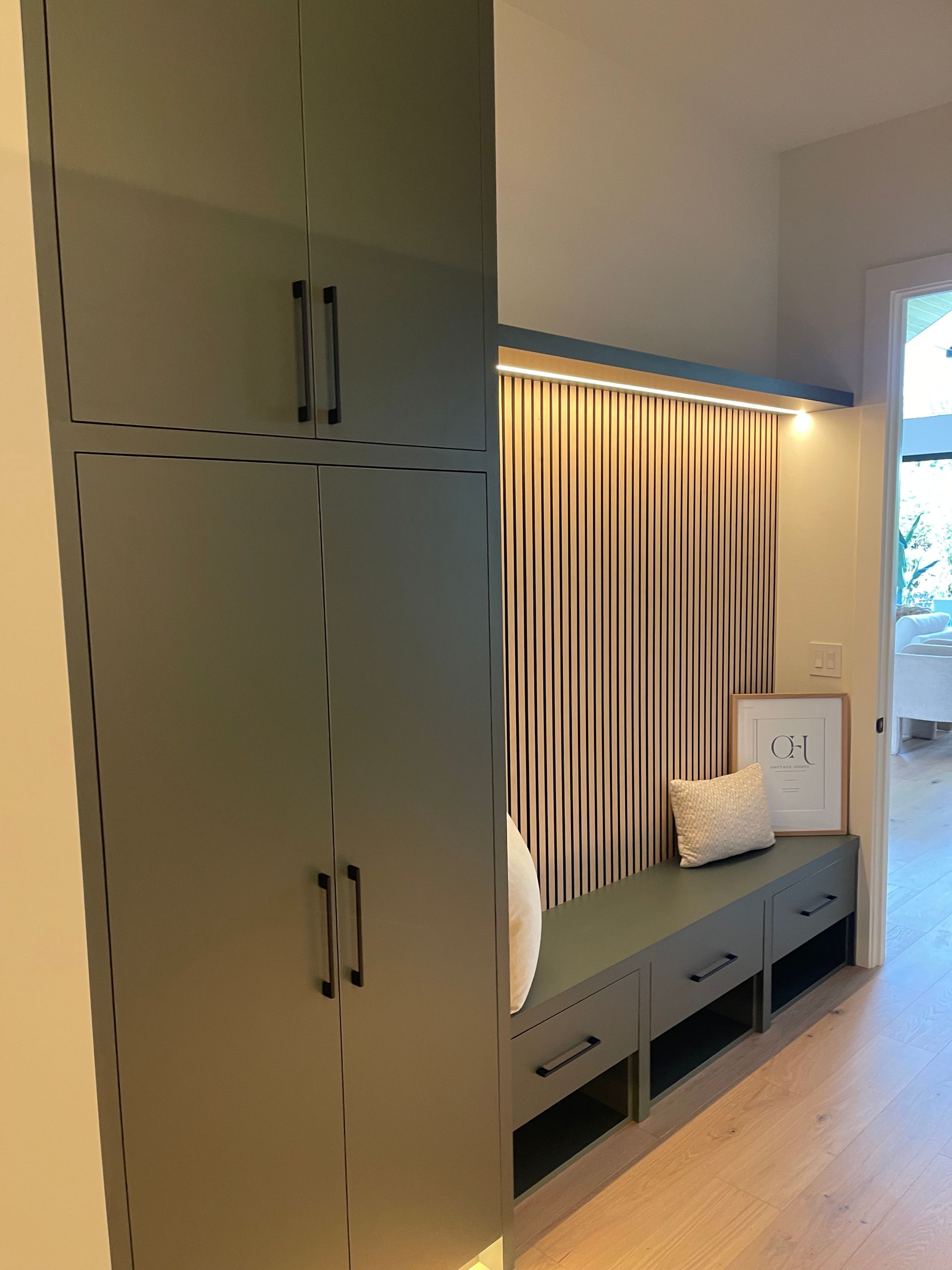 Modern laundry with built-in cabinets, long storage bench, curtains, and a window overlooking greenery in Portland,