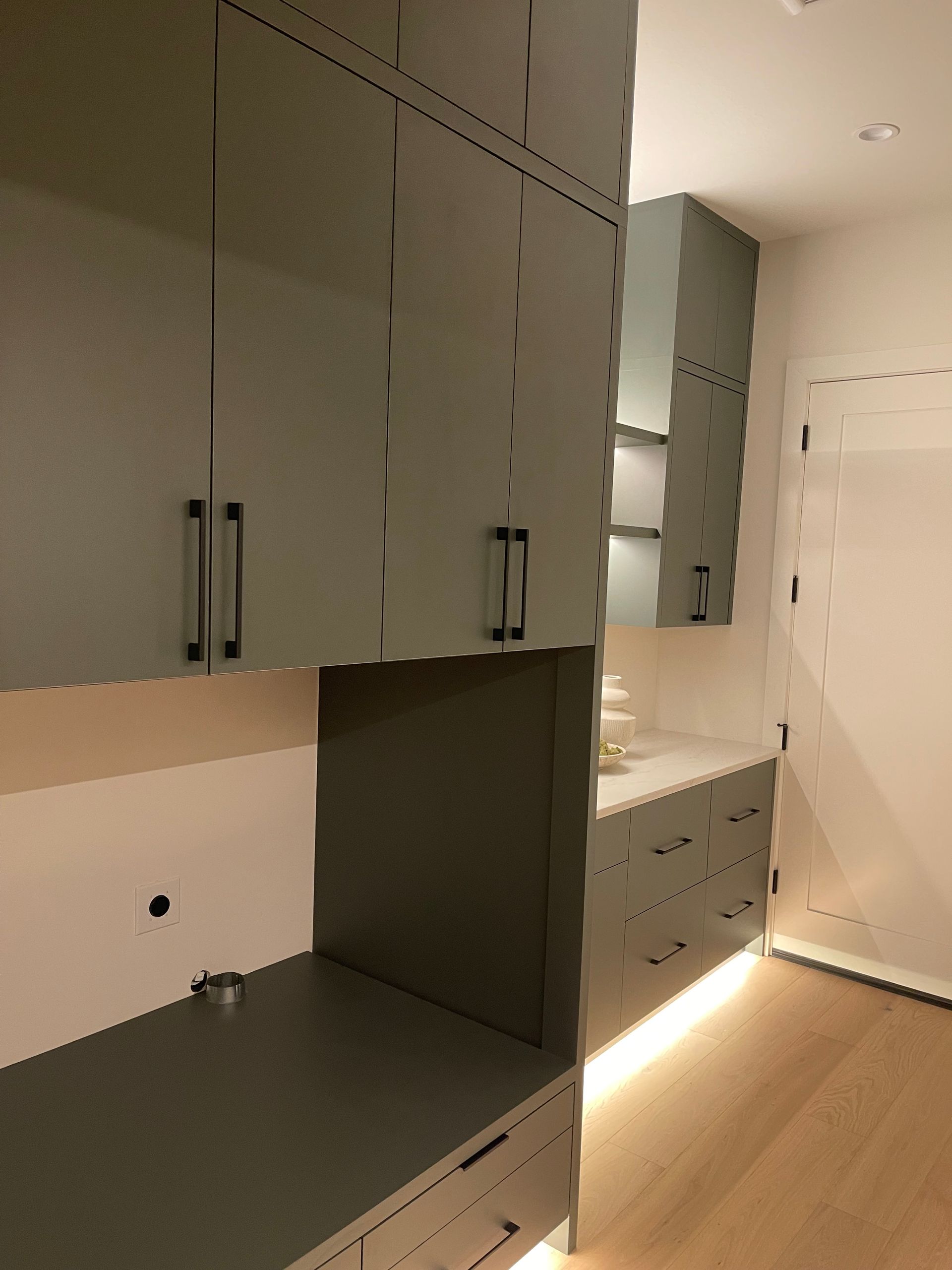Modern laundry with gray cabinets, dark countertops, and built-in appliances along a narrow hallway.