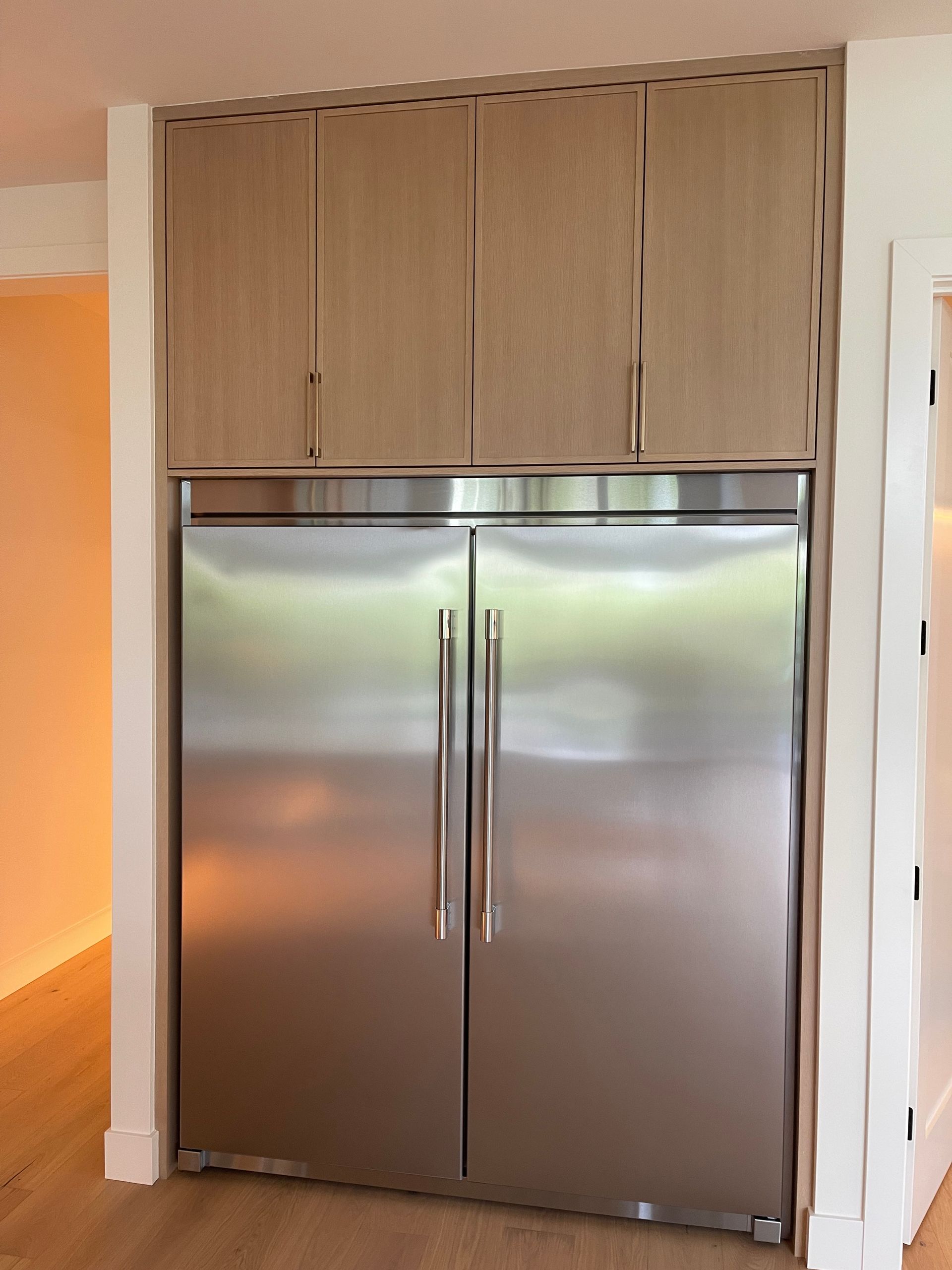 Built-in stainless steel double-door refrigerator under light wood cabinets in a kitchen nook