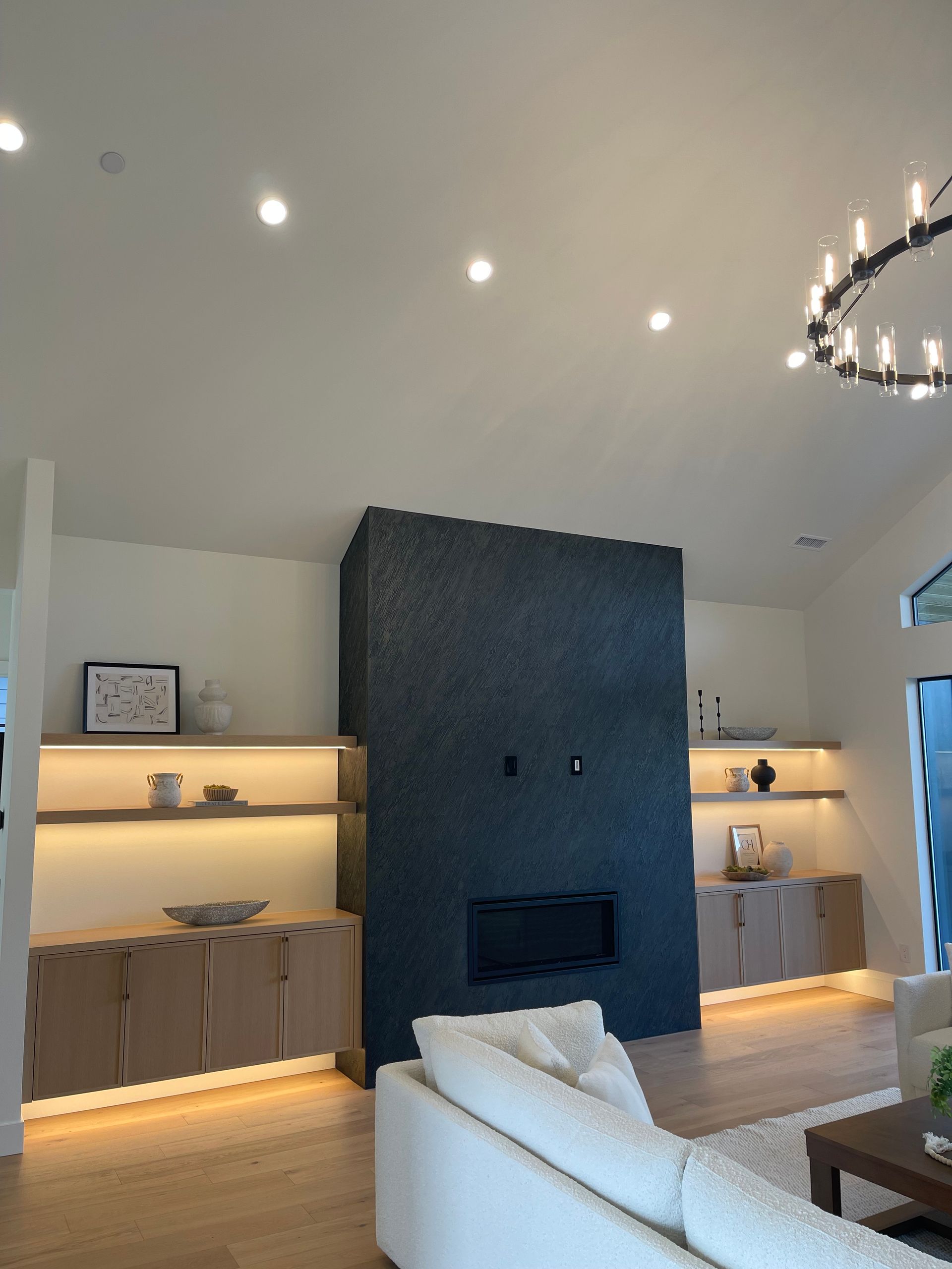 Modern living room with built-in shelves, dark stone fireplace, white sofa, and recessed ceiling lights.in Portland, Oregon