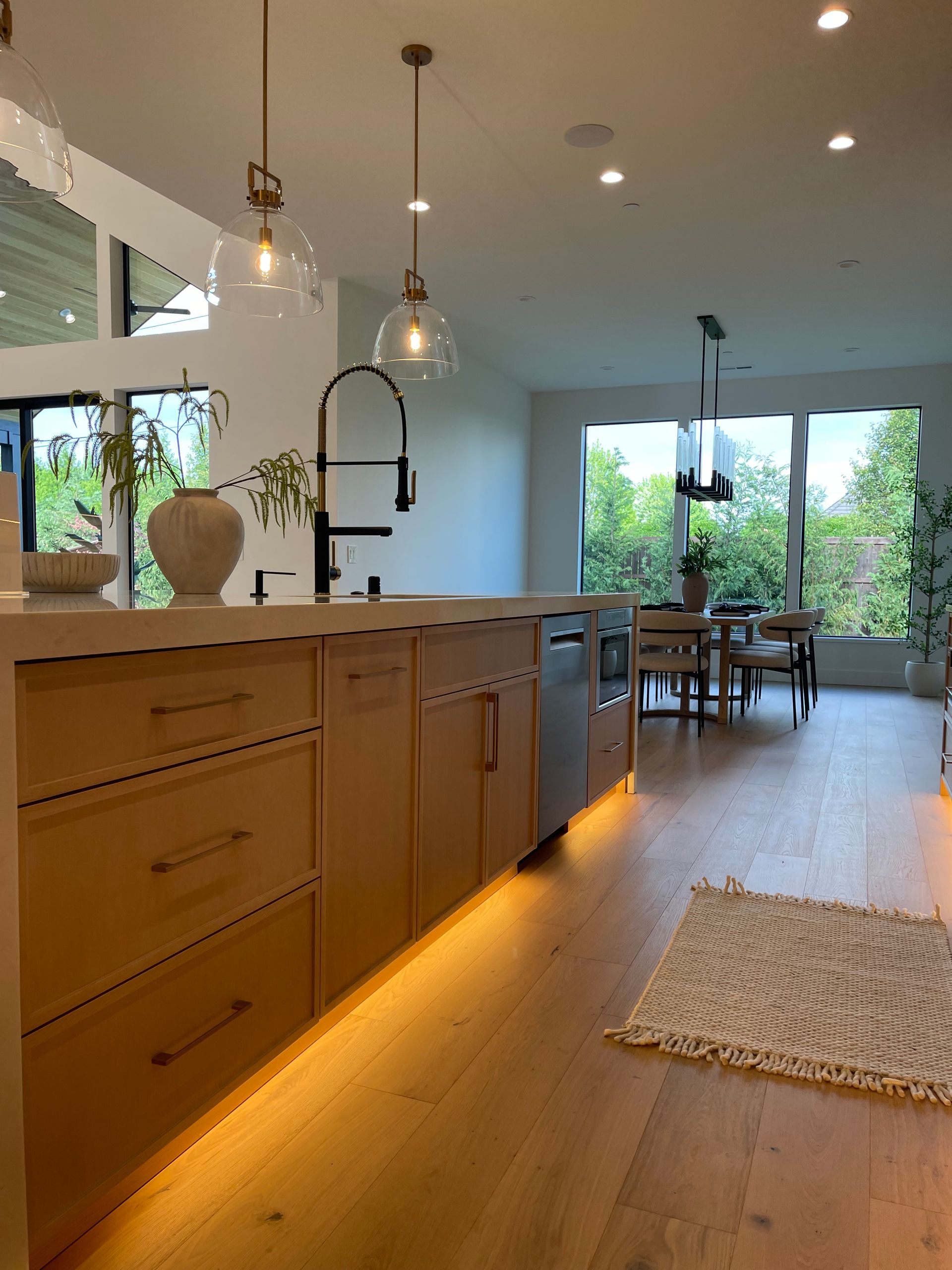 Bright modern kitchen with wood island, pendant lights, and dining area by large windows