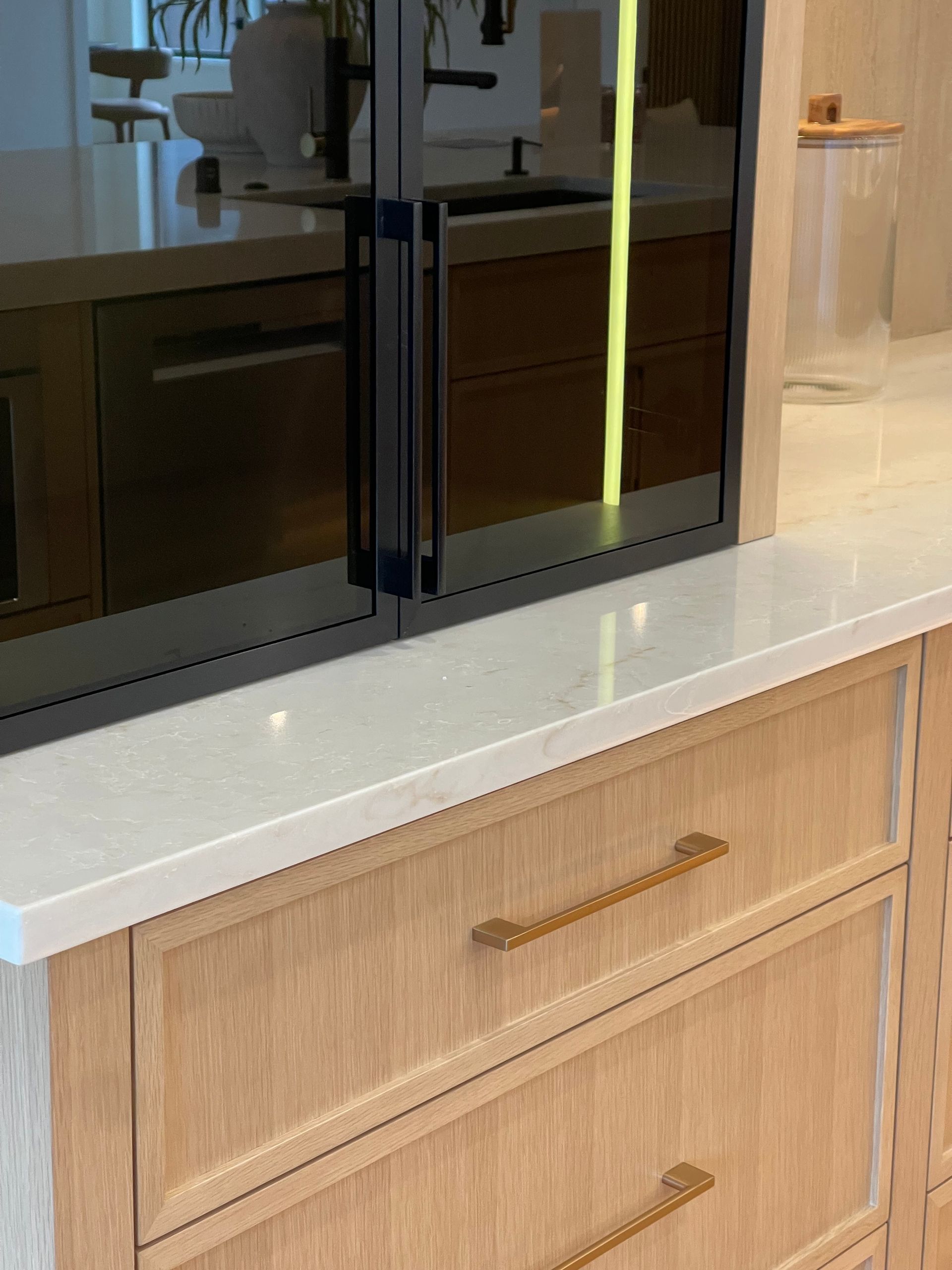White countertop with light wood drawers and gold handles beneath a black double-door appliance.