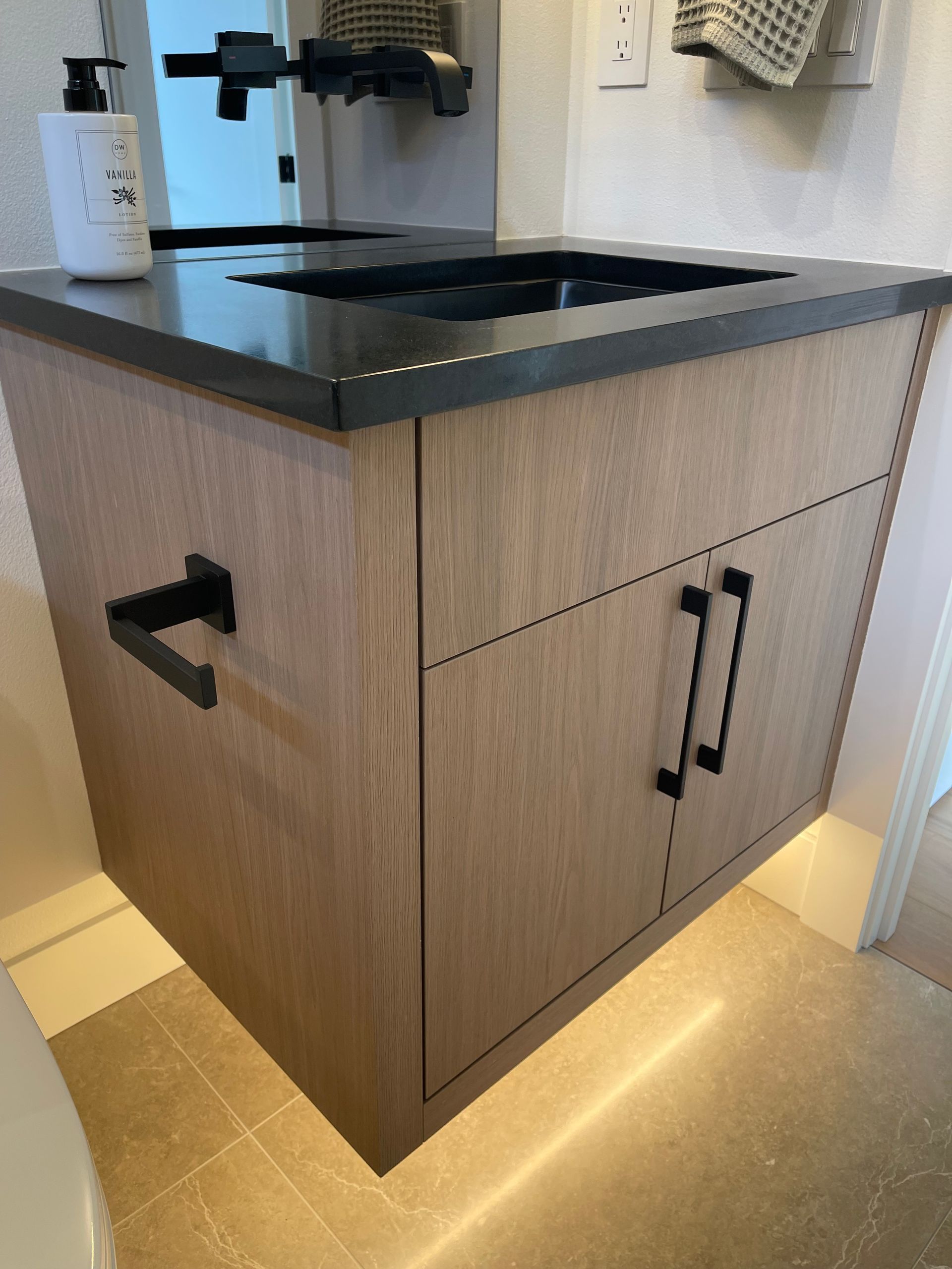 Modern wood vanity with black countertop and sink in a bathroom, lit from below in Portland, Oregon, WA