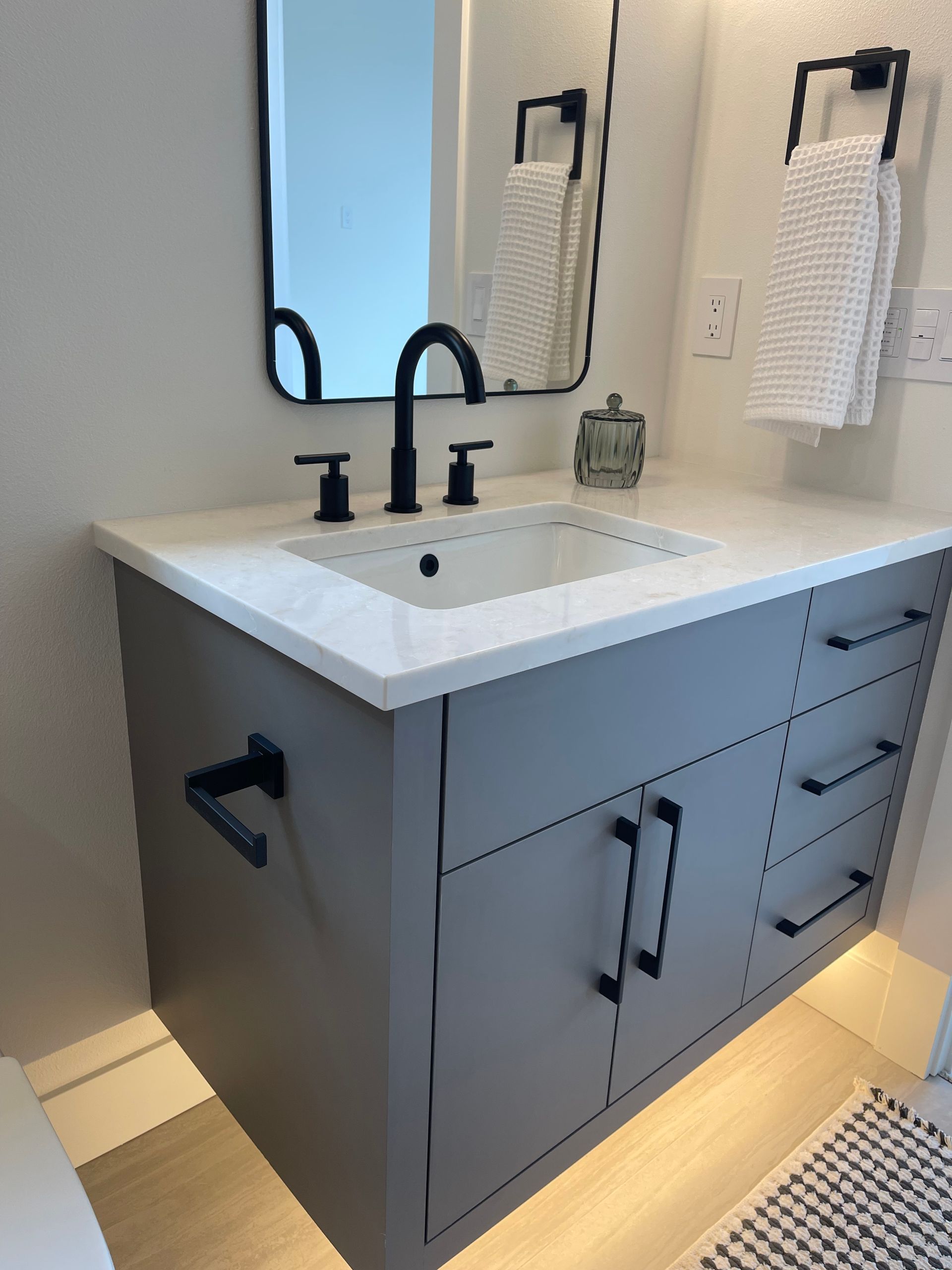 Modern gray bathroom vanity with white countertop, black faucet, mirror, and under-cabinet lighting in Portland, Oregon, WA