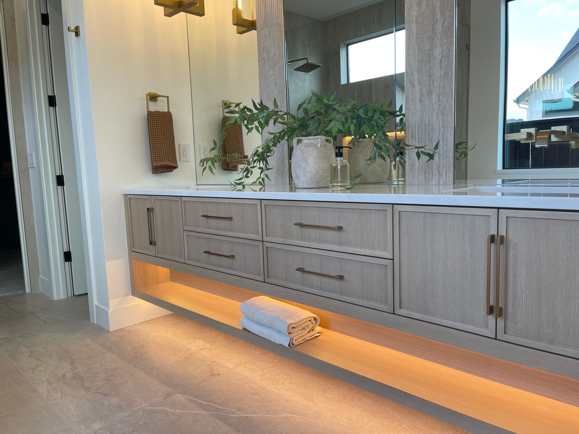 Modern bathroom vanity with light wood cabinets, white countertop, plants, and warm under-cabinet lighting in Portland