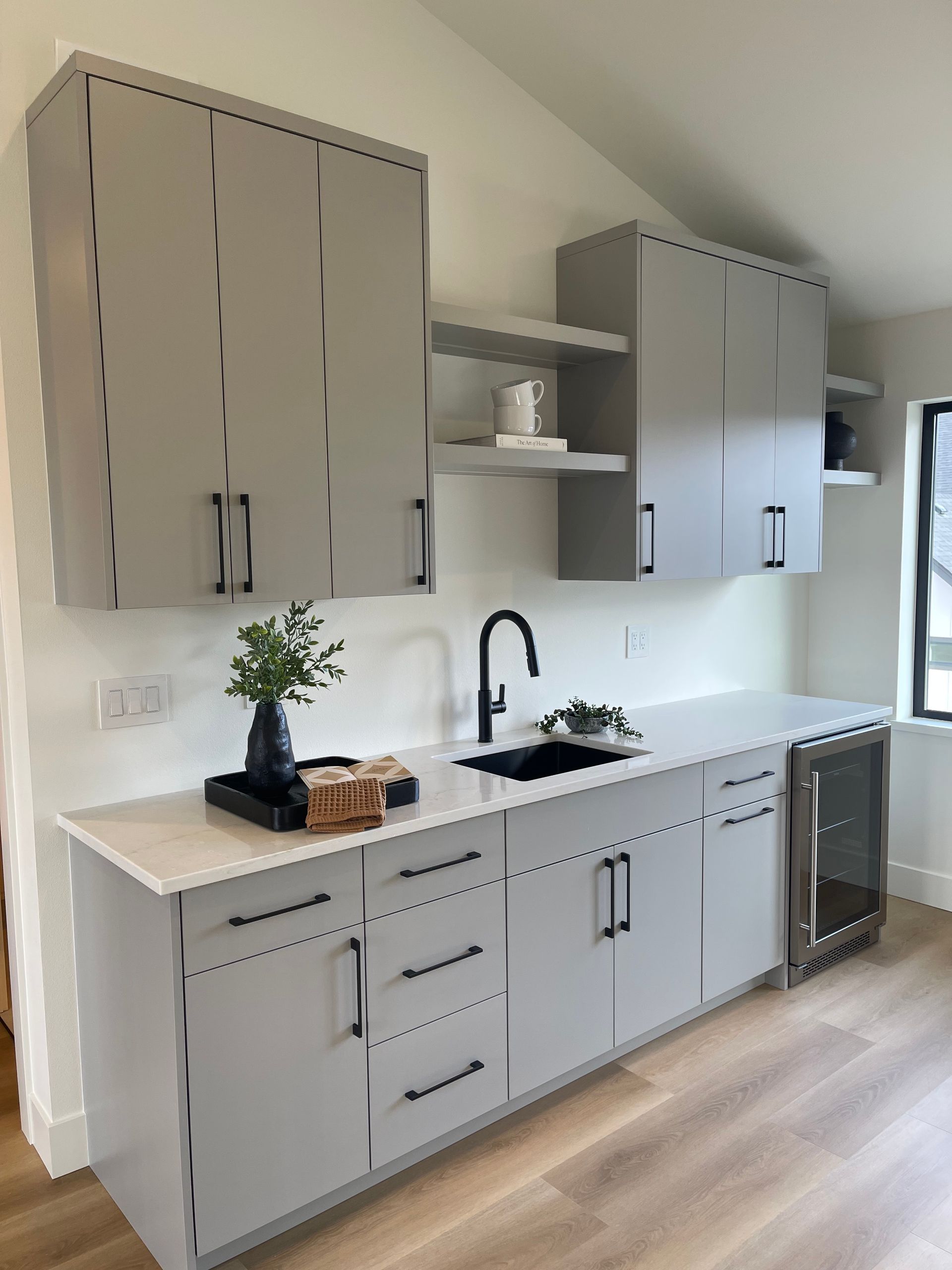 Modern gray kitchen cabinetry and white countertop with sink, stove, and wood flooring under pendant light