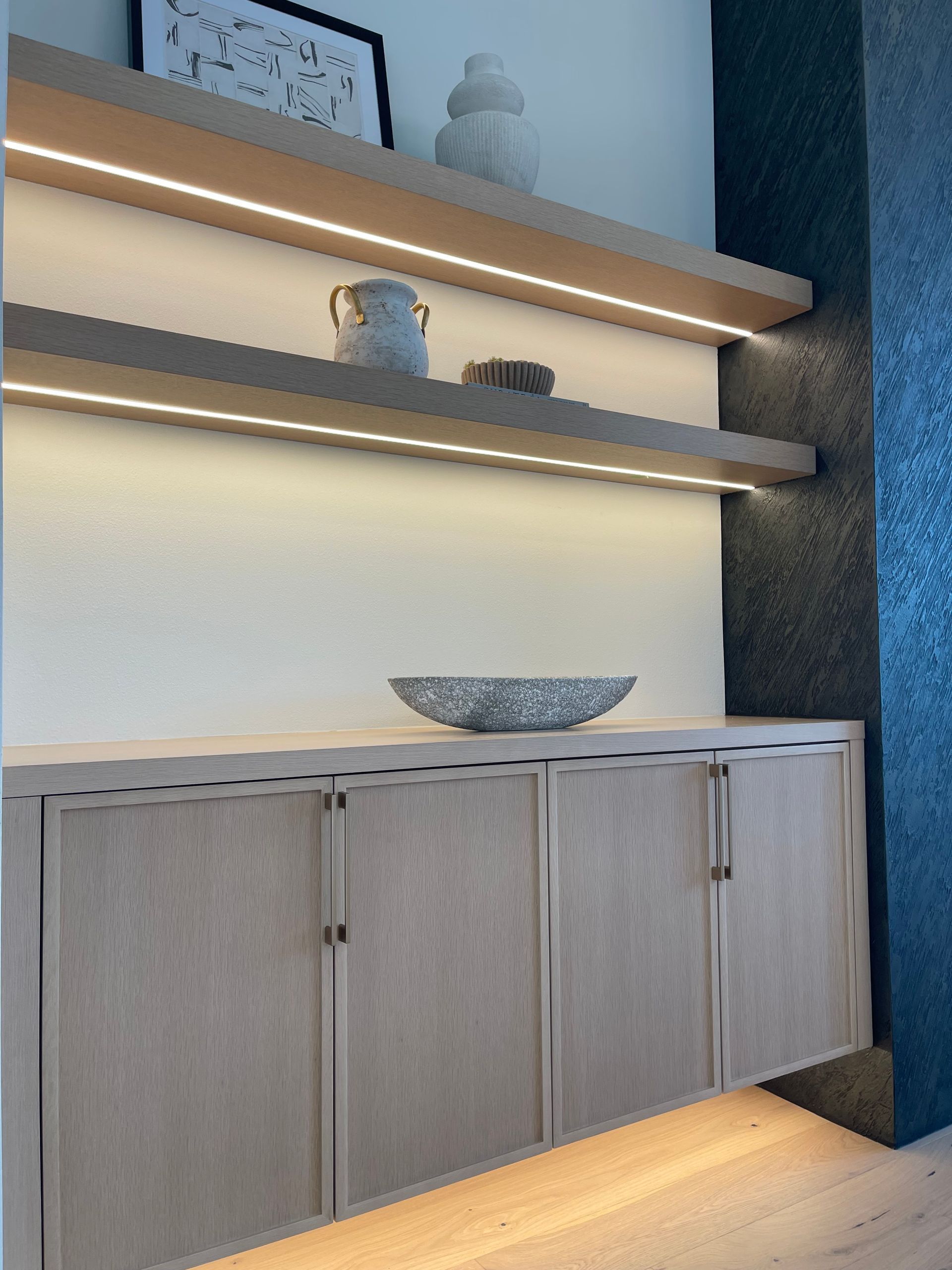 Modern cabinet with wood doors, floating shelves, and decorative bowls in a softly lit interior niche