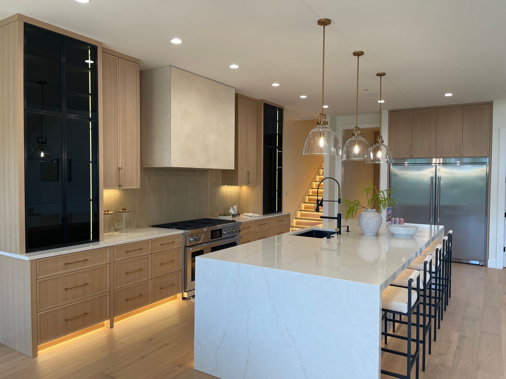 Modern kitchen with white island, wood cabinetry, pendant lights, and stainless steel refrigerator