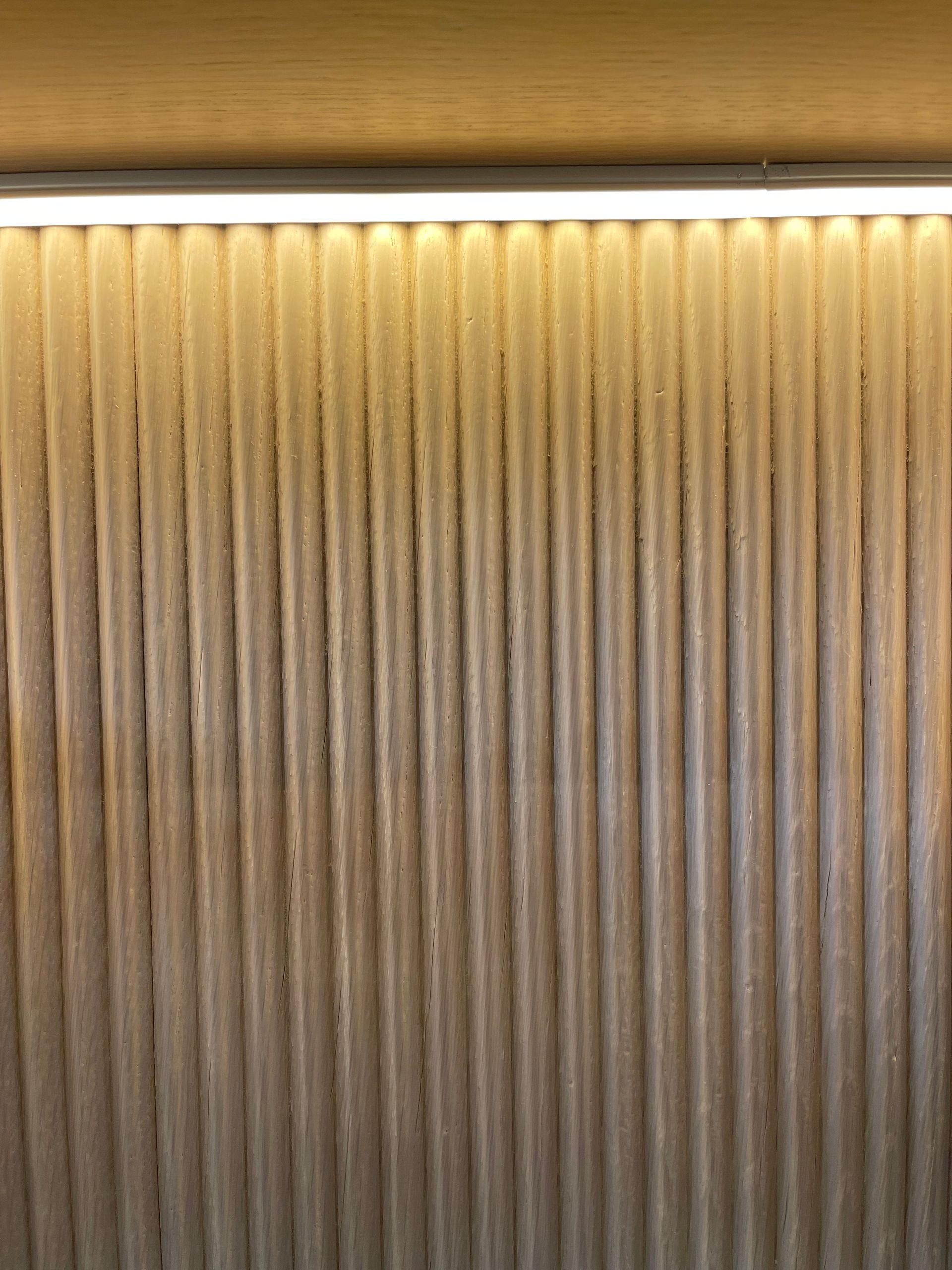 Warmly lit vertical ridged wall panel with a light strip along the top