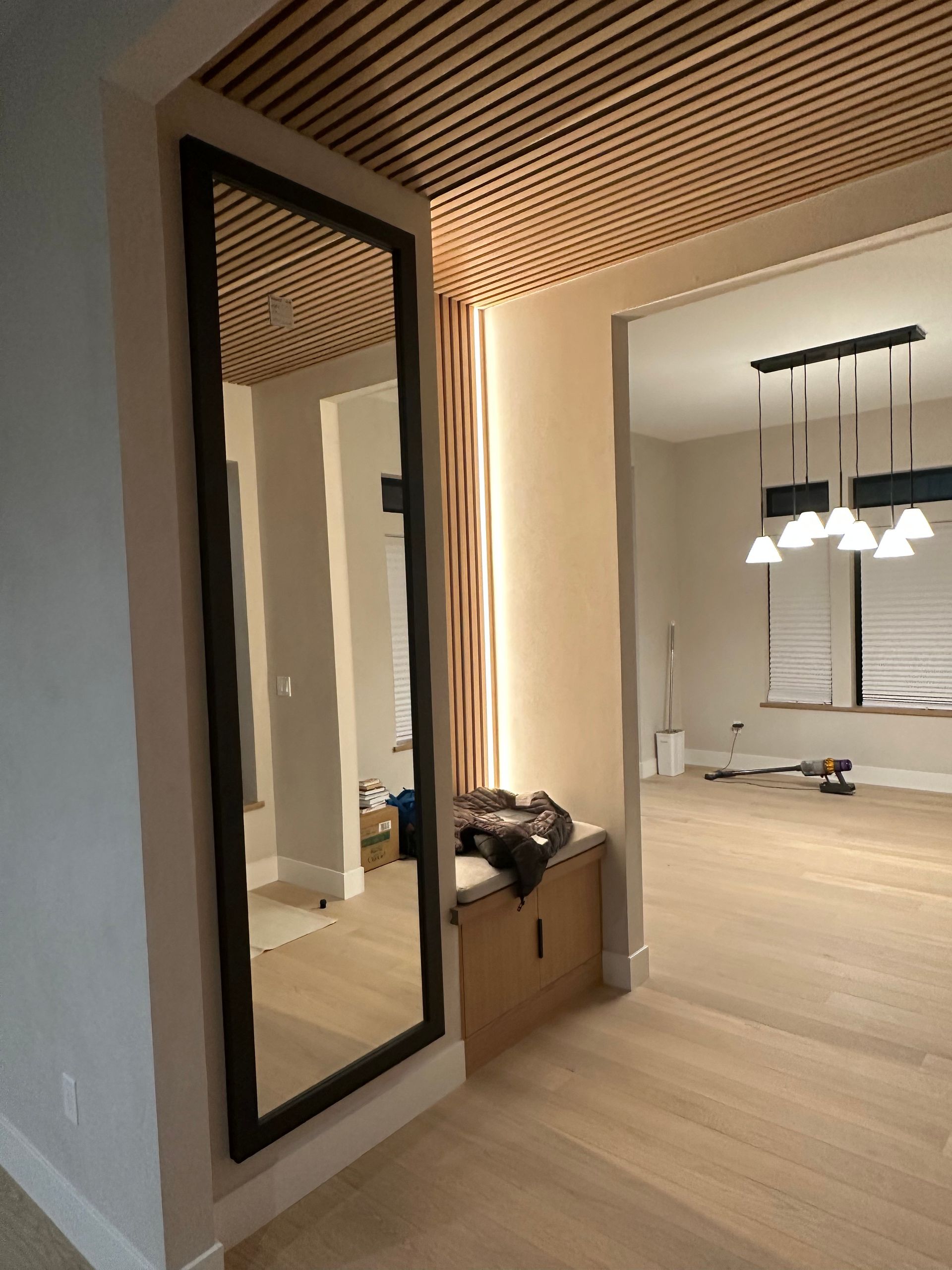 Modern hallway with a large mirror, wood slat ceiling, and open view into a lit dining room