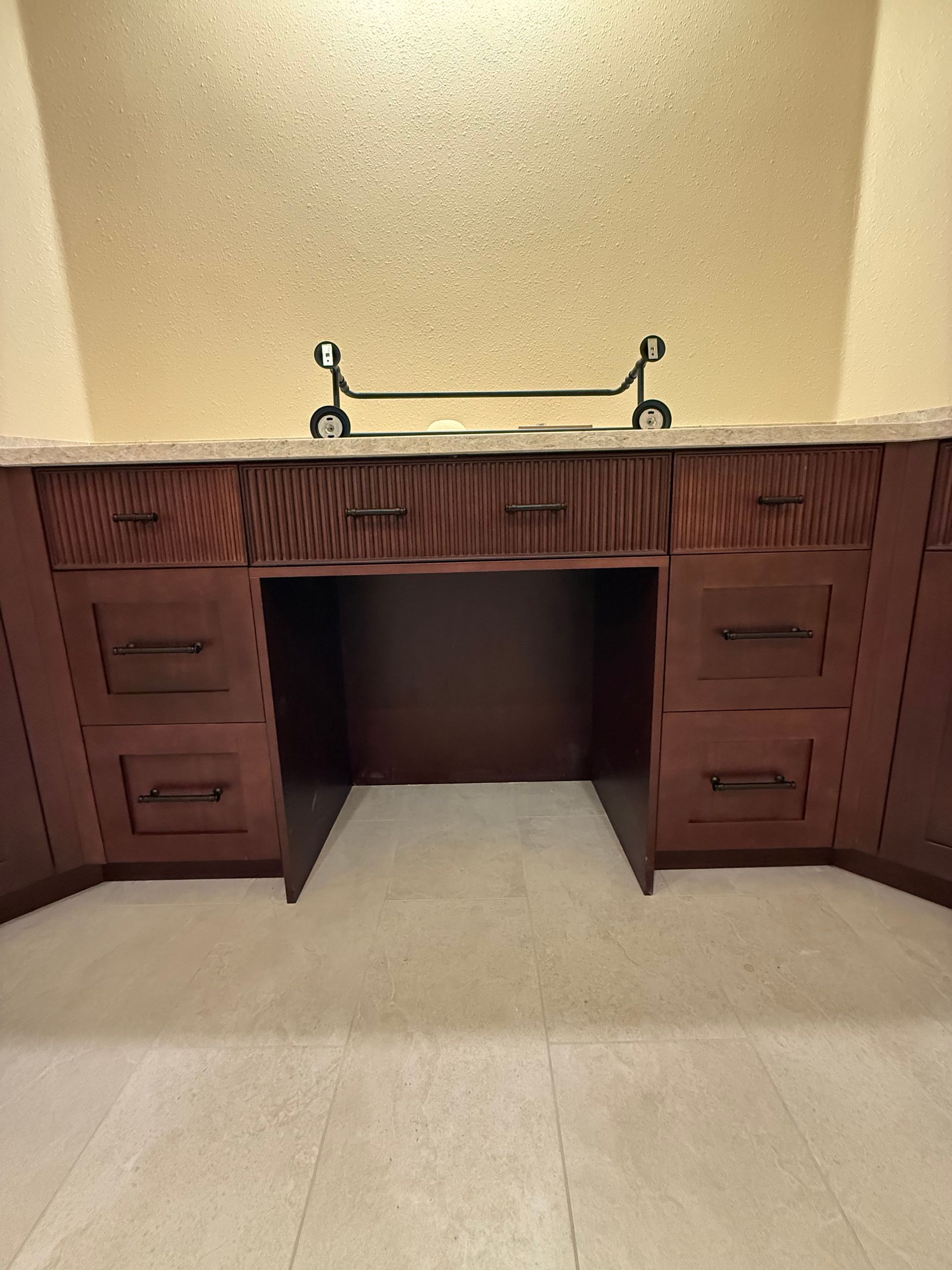 Dark wood bathroom vanity with drawers, open center area, light countertop, gold textured wall.