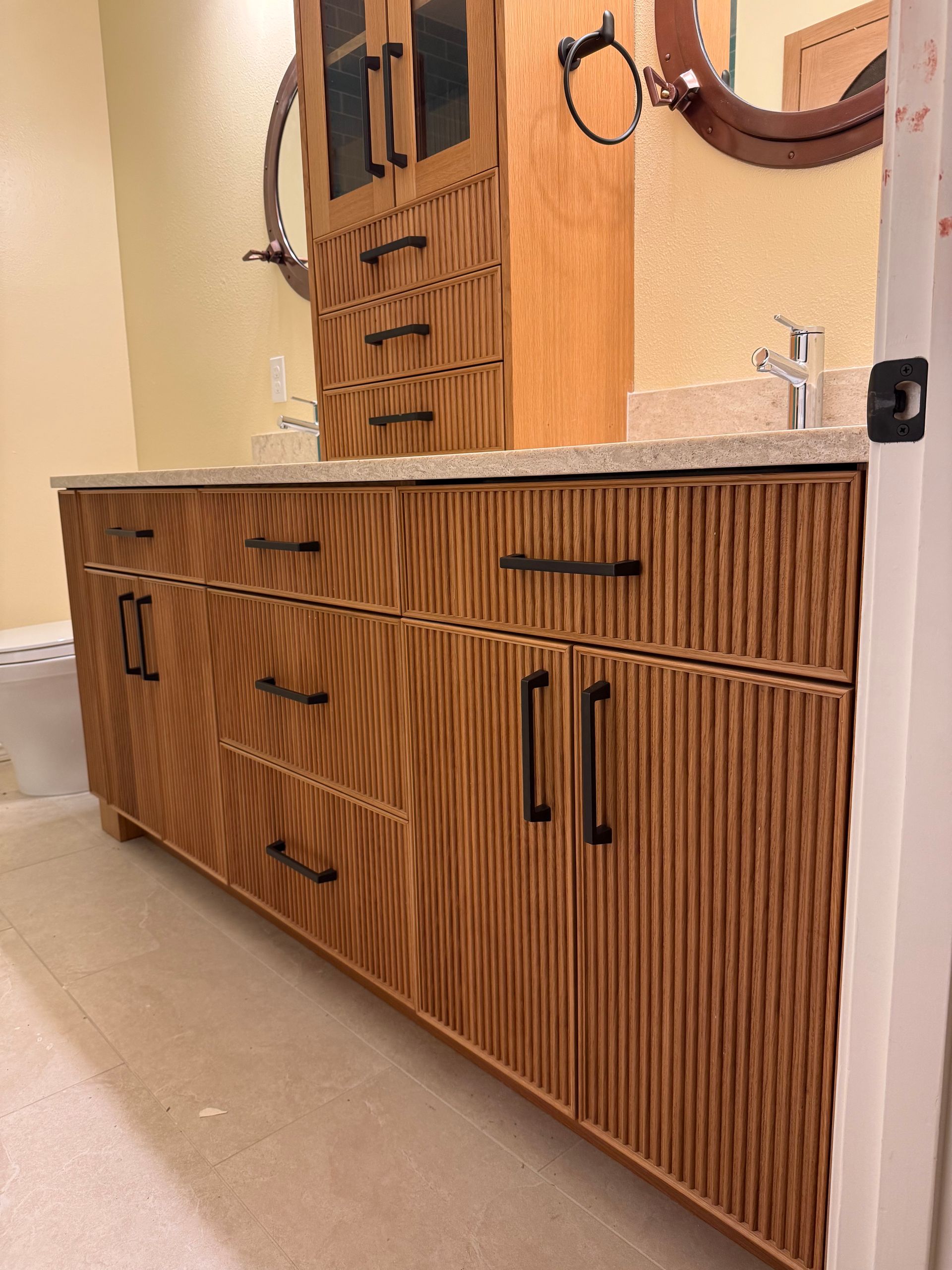 Wooden bathroom vanity and cabinet with a ribbed texture, black hardware, and a stone countertop.