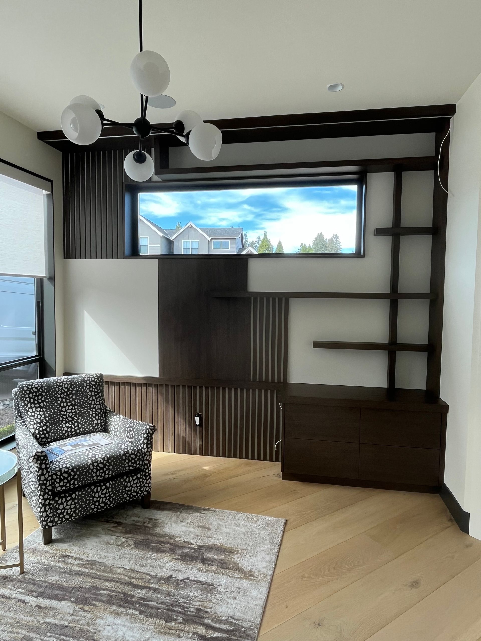 Room with dark wood built-in shelving, a window, patterned chair, and a rug on a hardwood floor.