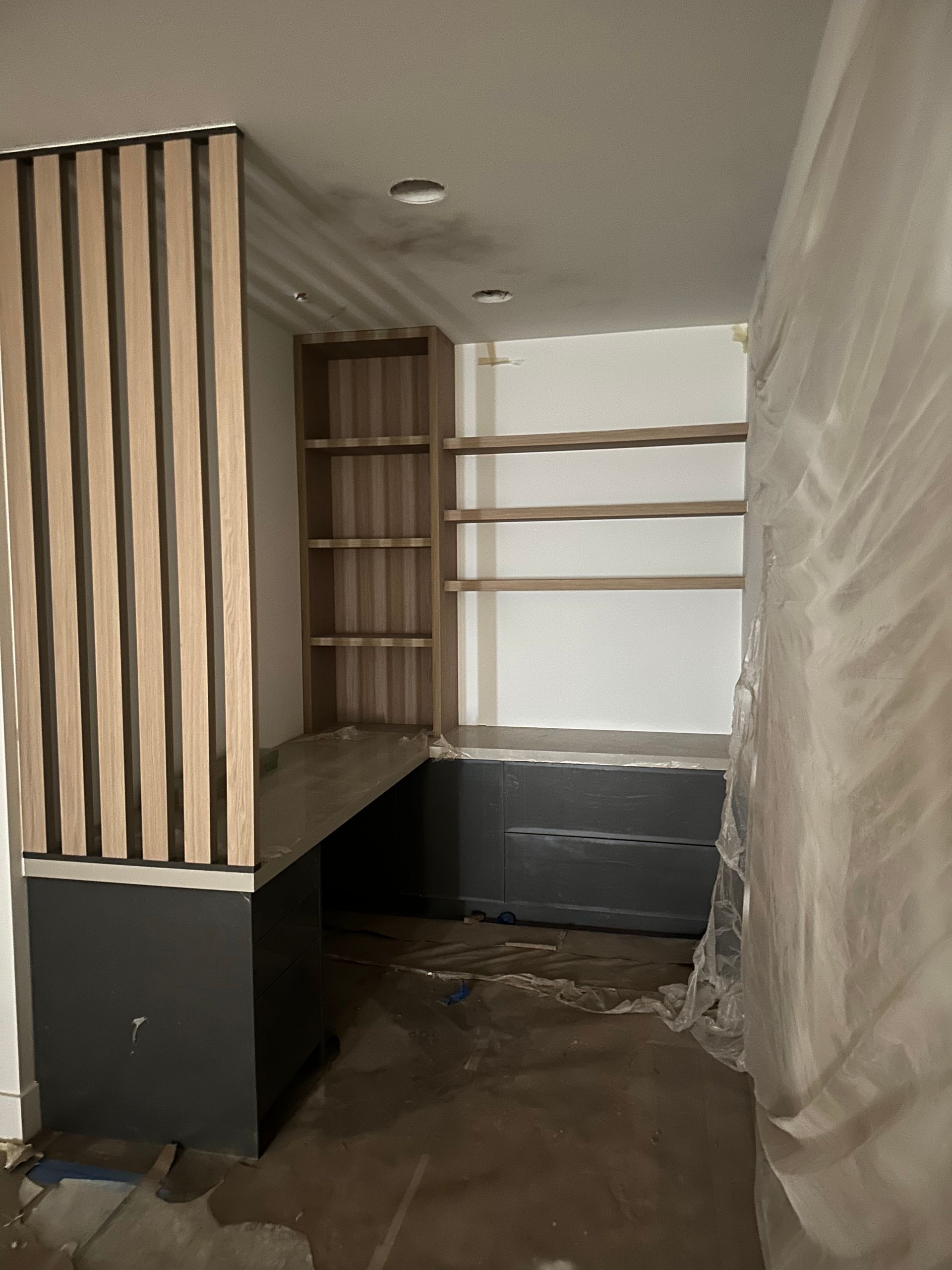 Unfinished room with wood shelving, black cabinets, and plastic sheeting on the right wall.