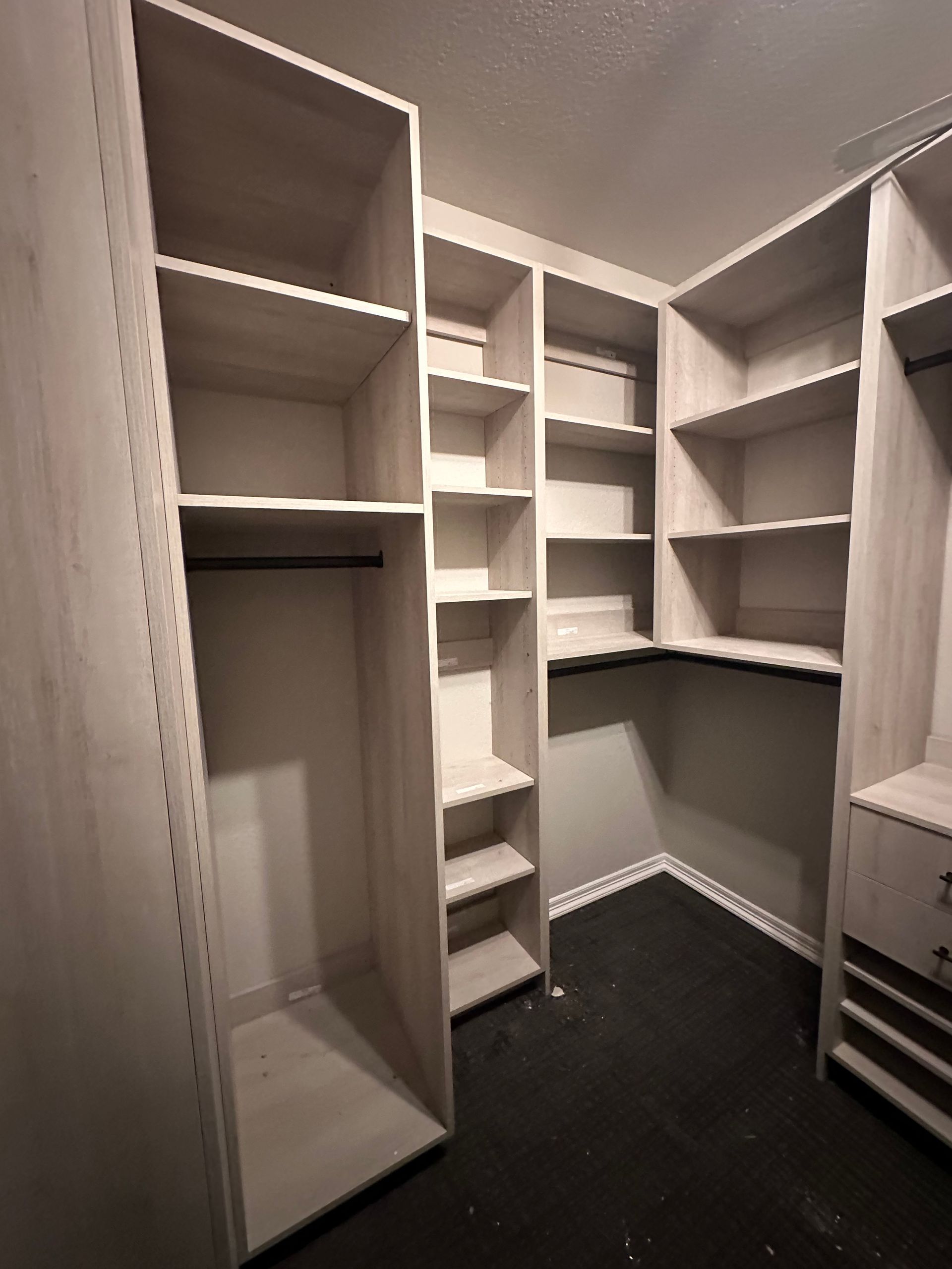 Empty walk-in closet with built-in shelving and hanging rods. Light-colored wood, dark floor.