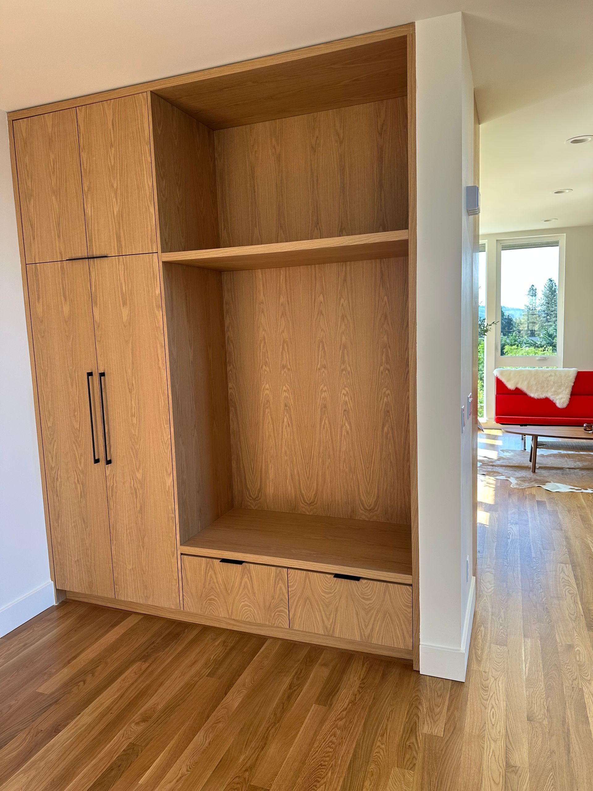 Built-in plywood cabinet with shelves and closed doors, against a white wall. Wood flooring.