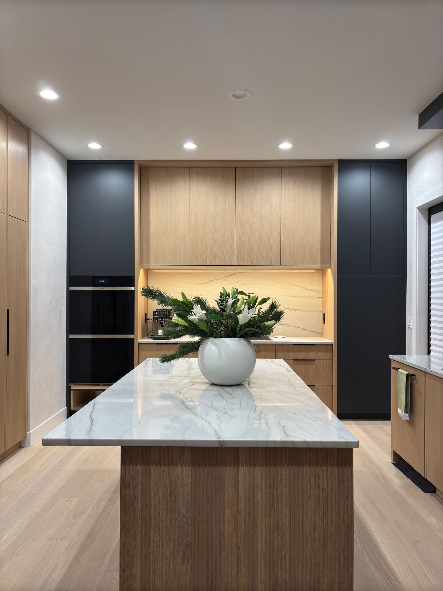 Modern kitchen with light wood cabinetry, marble island, and dark gray accent walls.