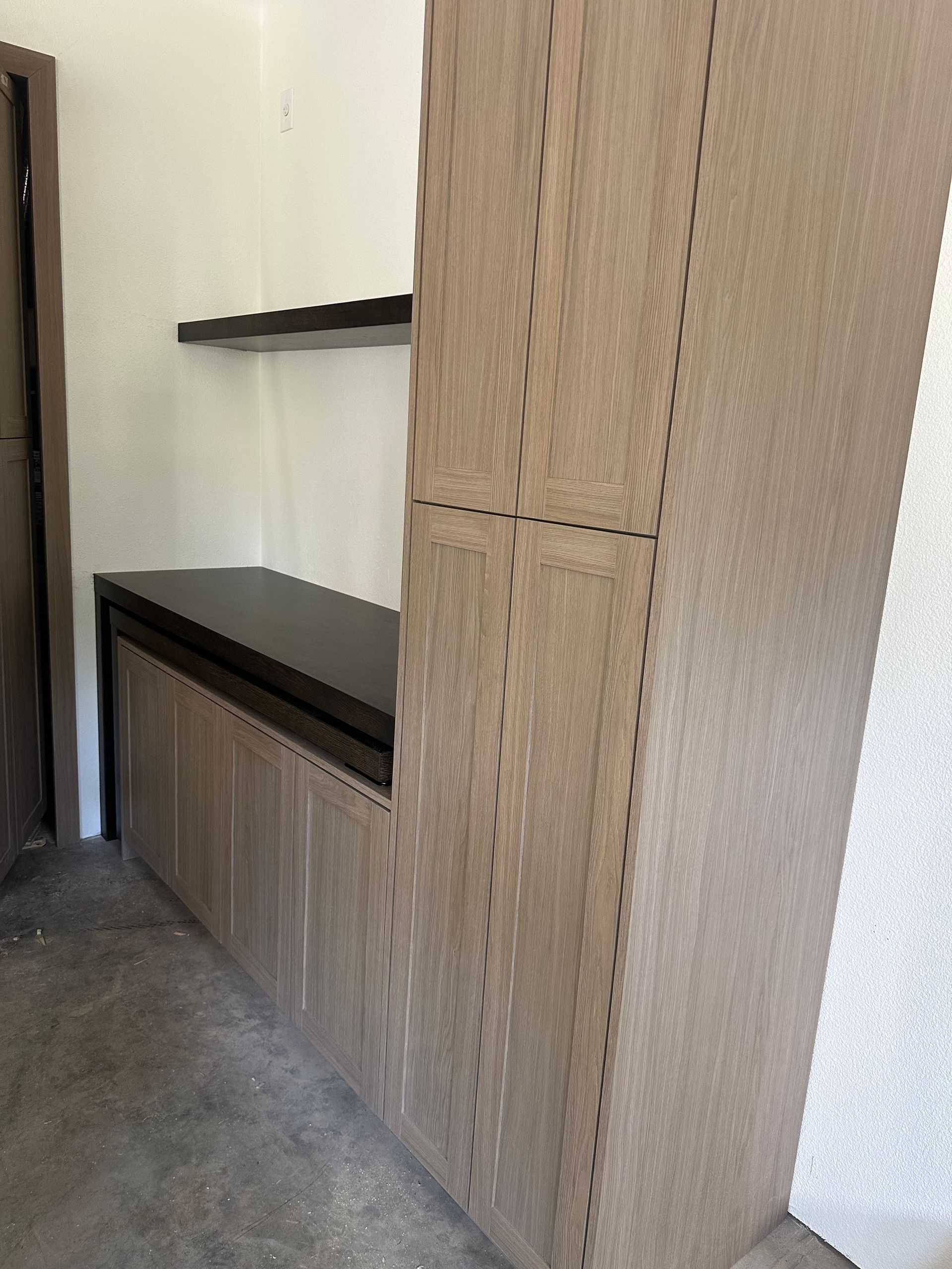 Cabinets with dark countertop and shelf against a white wall.